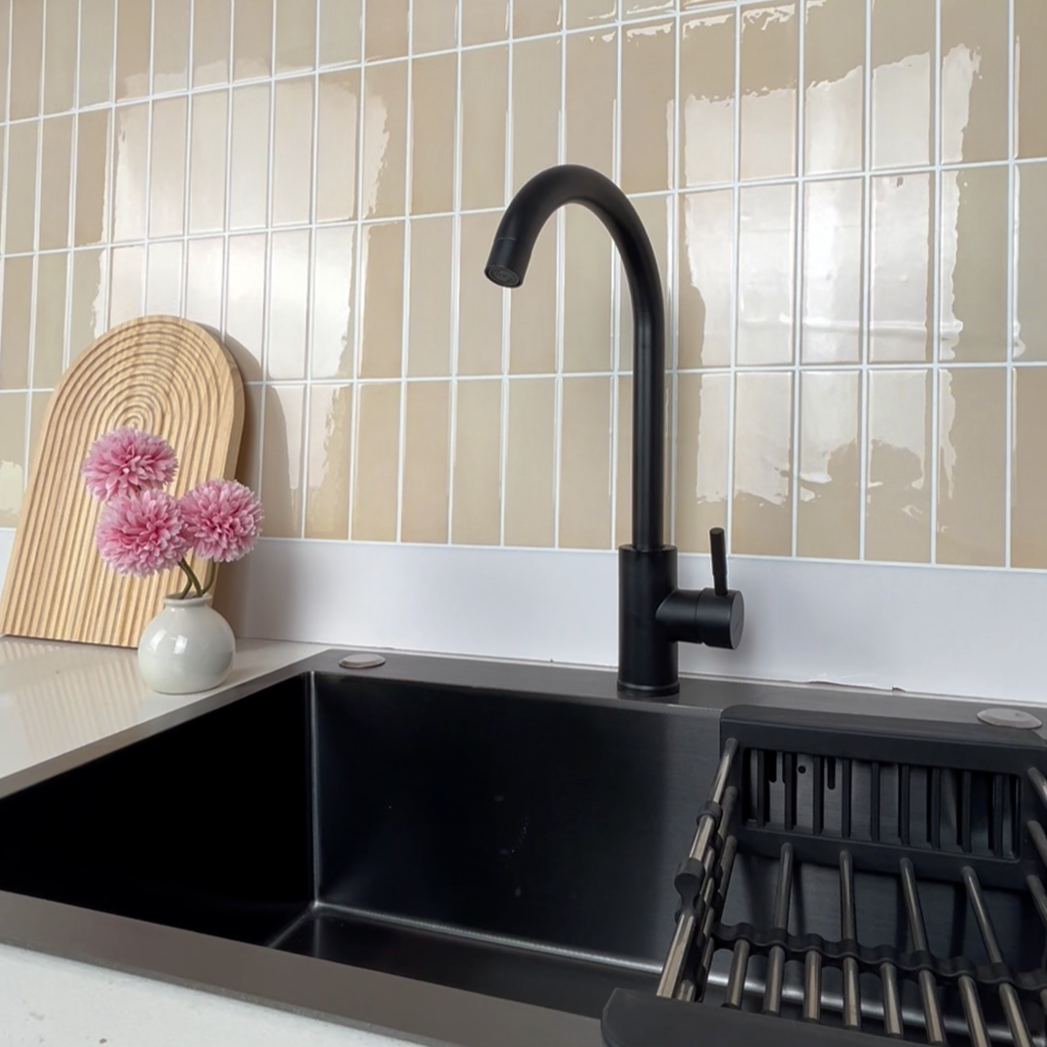 Black kitchen sink with faucet against a beige tiled wall