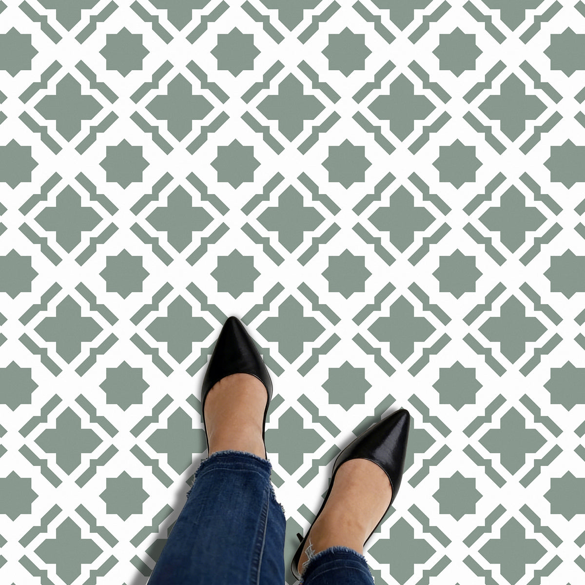 Person wearing black shoes and blue jeans standing on a patterned floor.