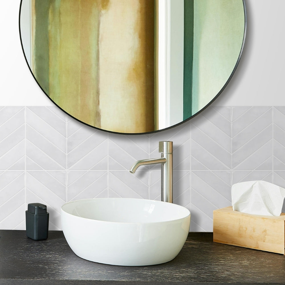 Bathroom vanity with round mirror, white sink and chevron tiels, and decorative elements.
