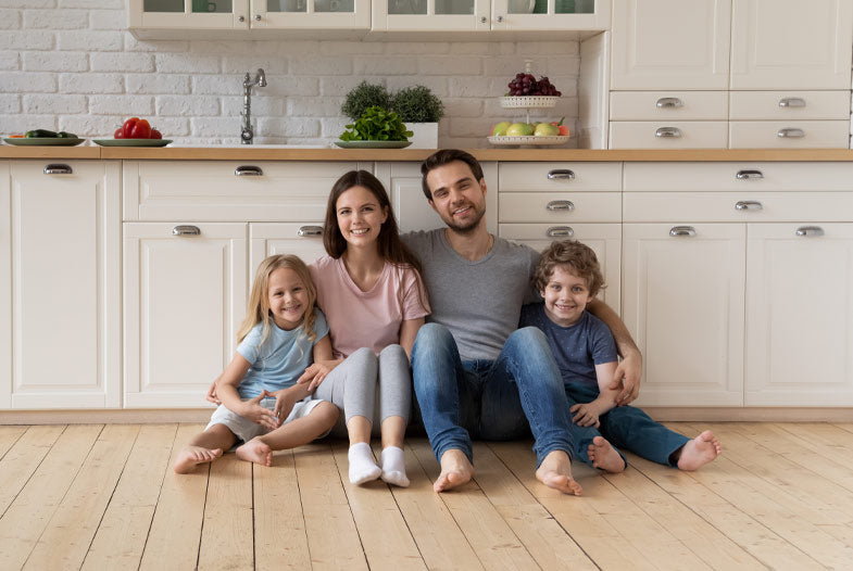 Happy young daughter, dad, son sitting on floor in front of white kitchen