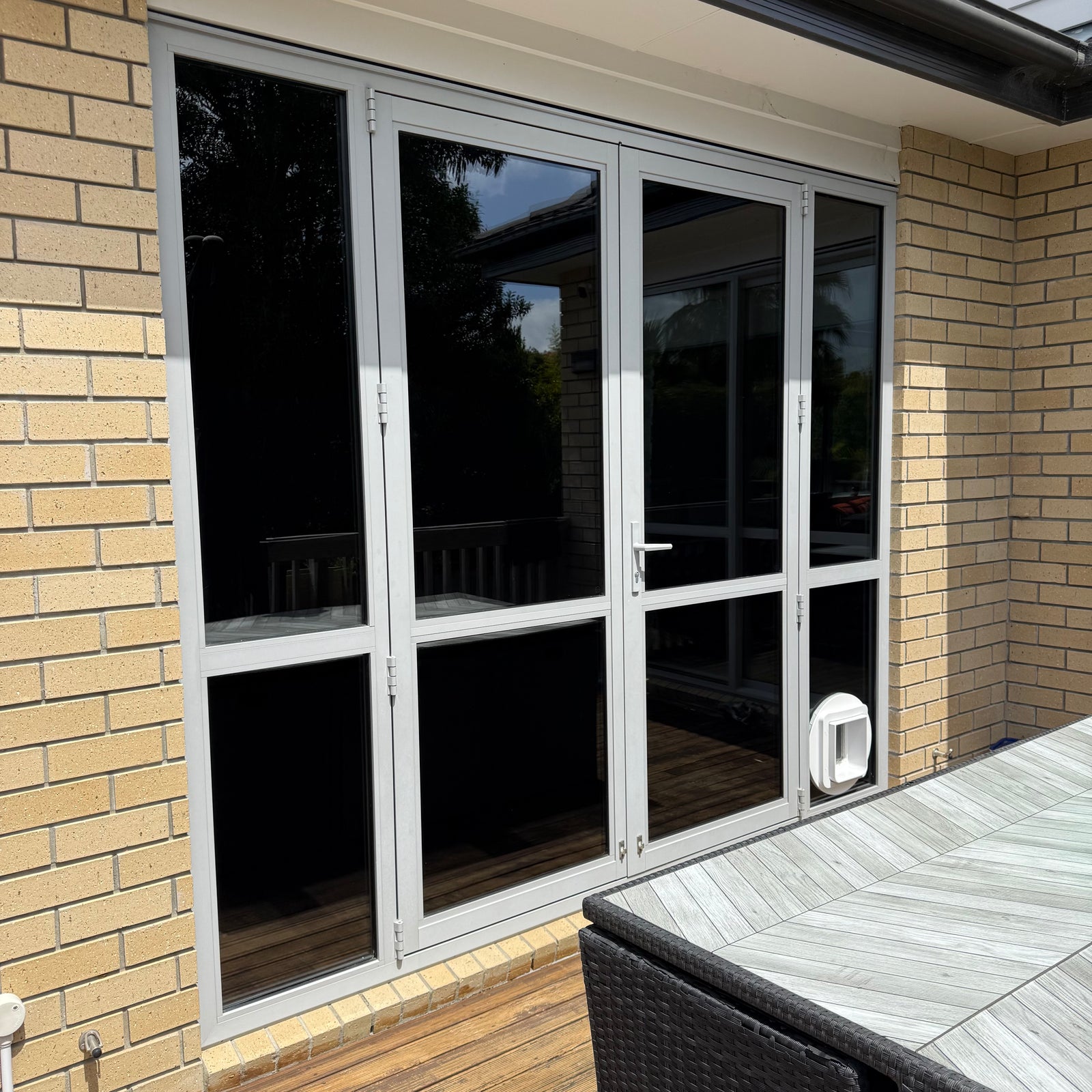 Bifold glass door with mirror effect film on a brick wall with outdoor furniture