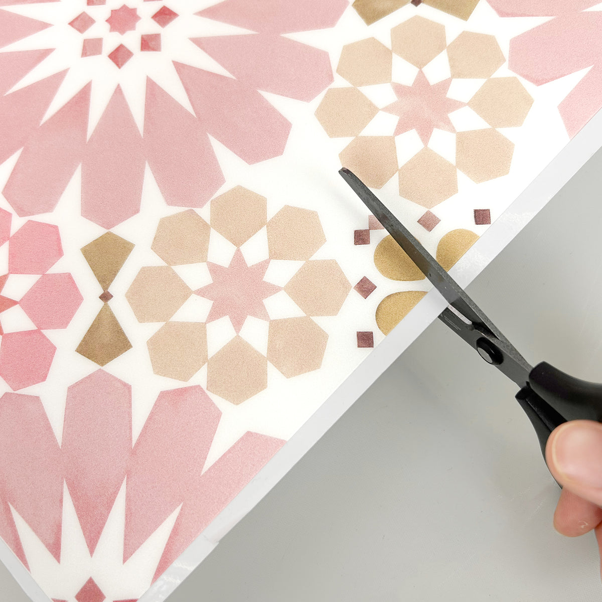 Scissors cutting through a floor tile with pink and beige geometric pattern