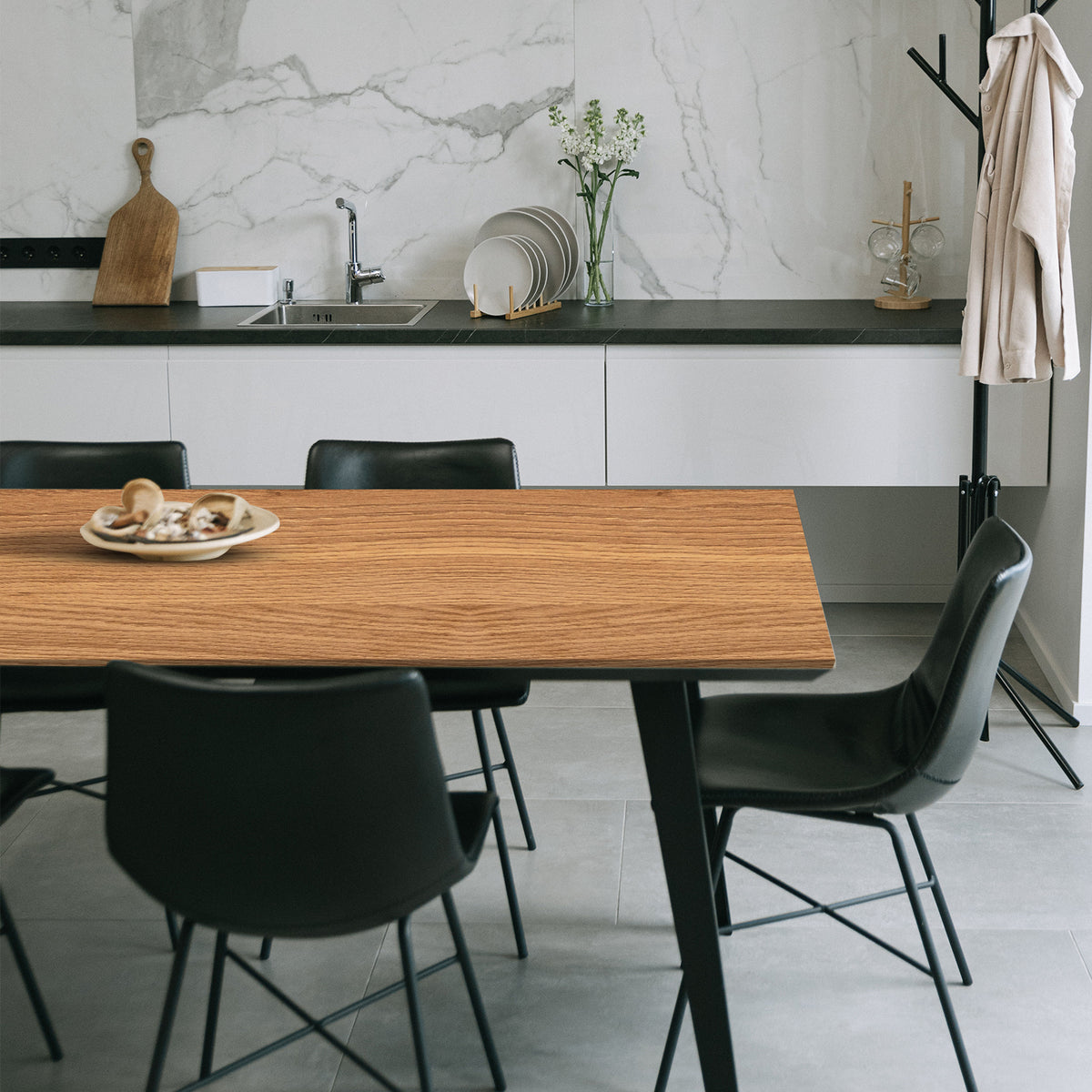 Modern kitchen with wooden vinyl wrapped dining table and black chairs, marble backsplash.