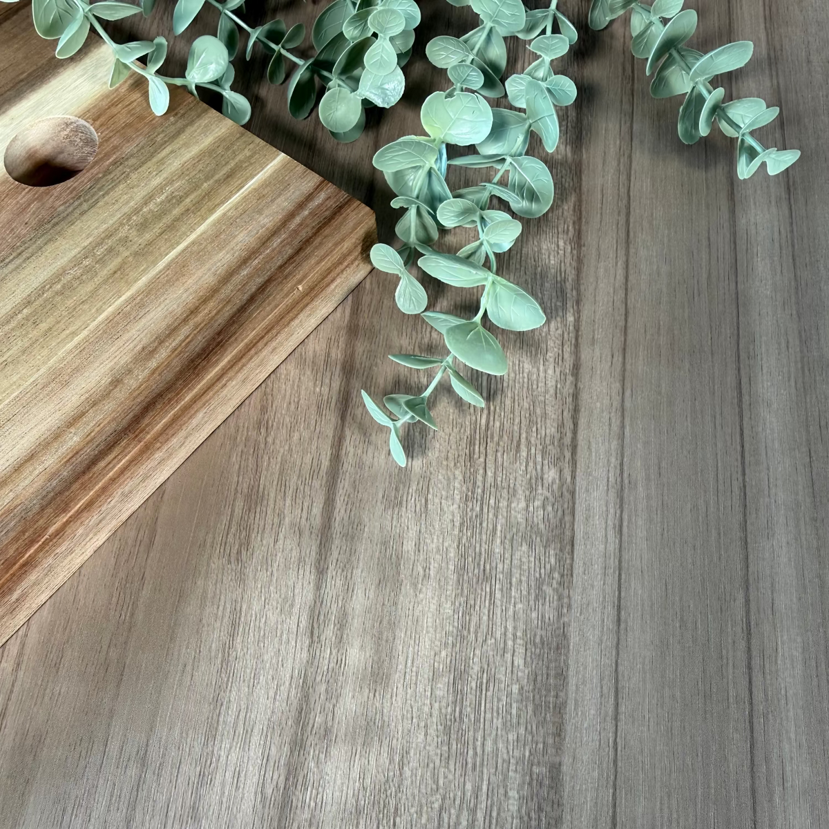 Wooden cutting board with a eucalyptus branch on a wooden adhesive vinyl bench top