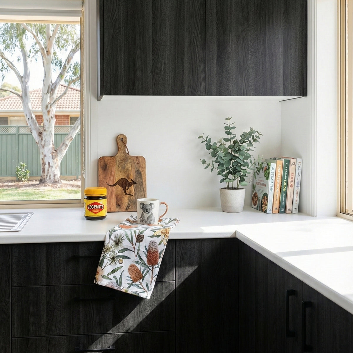 Modern kitchen with black oak vinyl wrapped cabinets, white countertops, and a window view of trees.