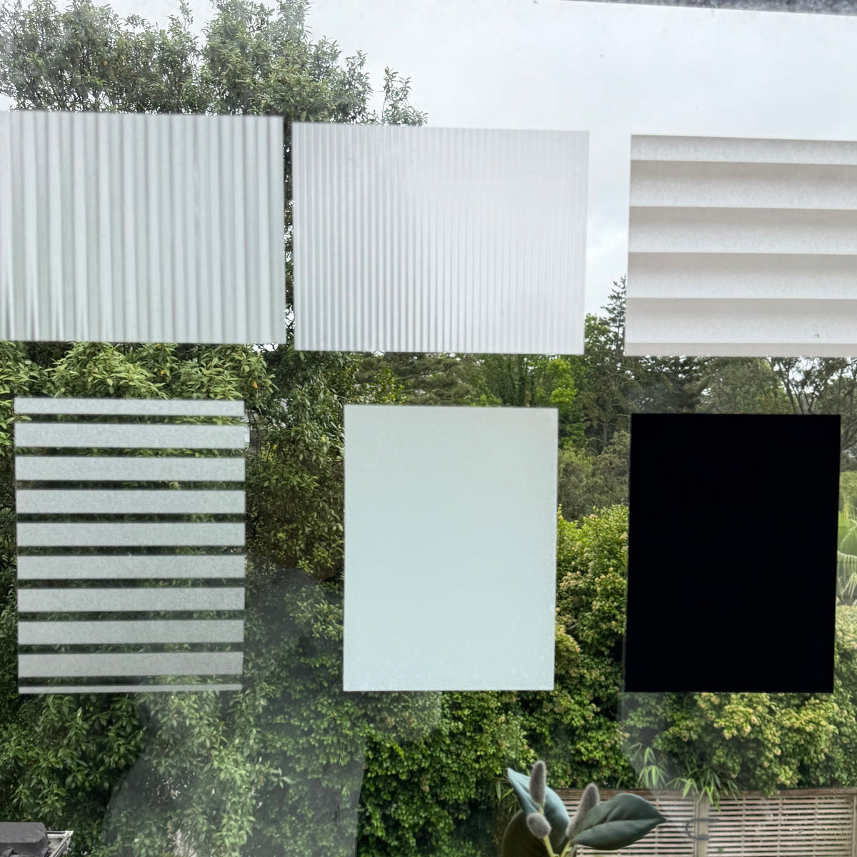 Collection of window film samples with different patterns and colors against a green outdoor background.