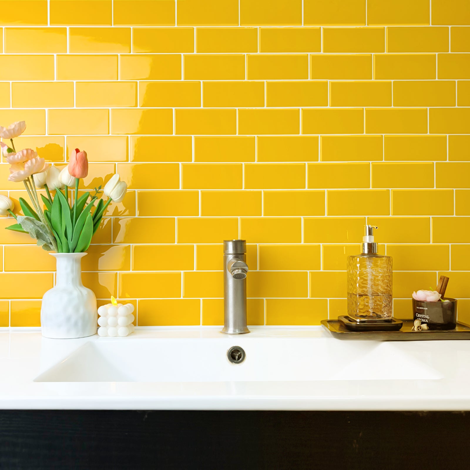 Bathroom sink area with yellow tiled wall and decorative items.