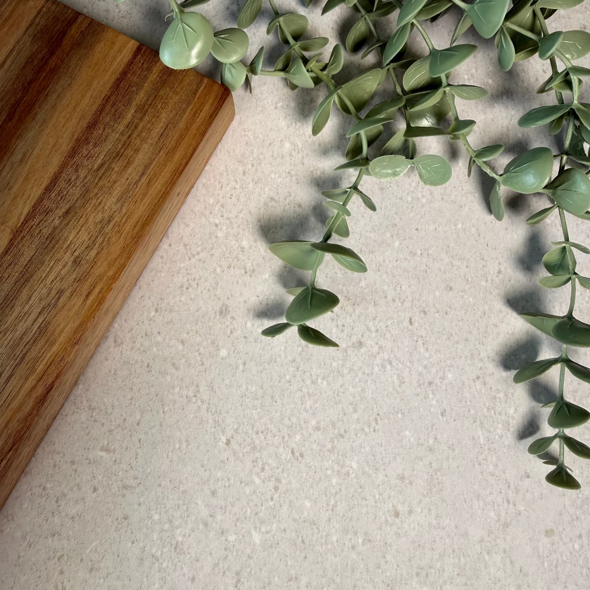 Green leaves on a light grey stone benchtop with a wooden shopping board edge