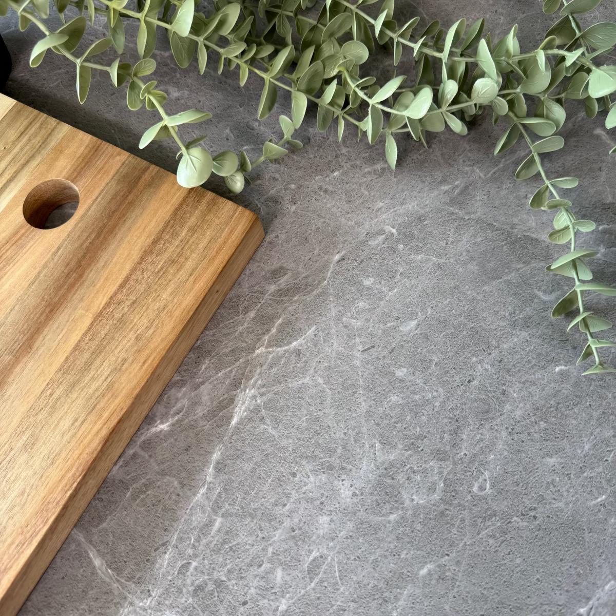 Wooden cutting board on a grey stone adhesive vinyl surface with green leaves.