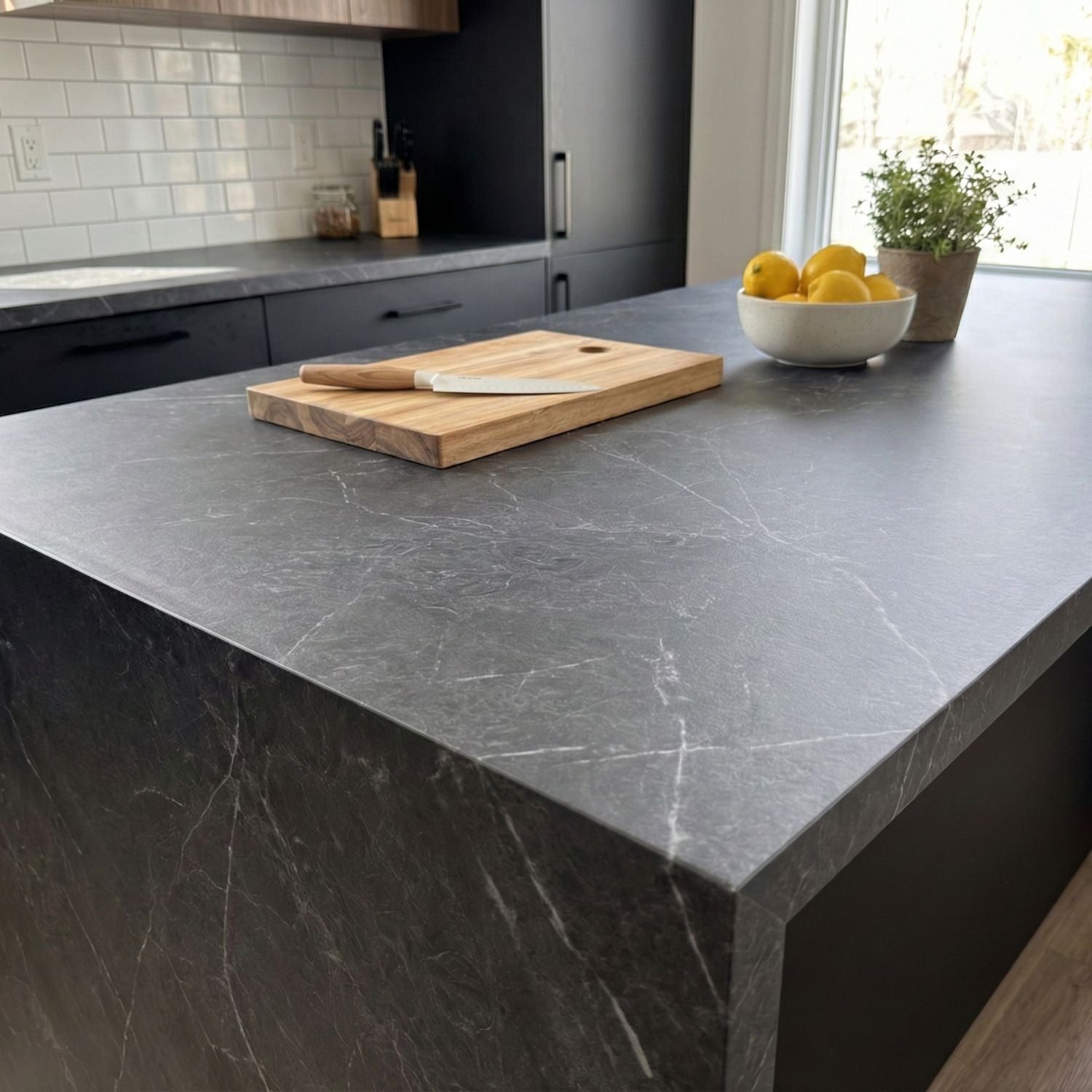 Grey marble vinyl wrapped countertop with a cutting board, knife, and bowl of lemons in a kitchen.