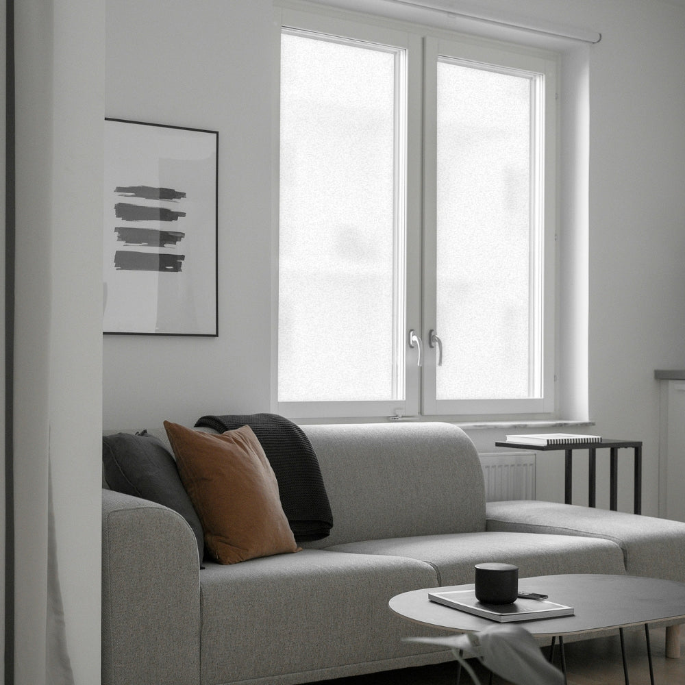 Modern living room with a gray sofa, coffee table, and frosted window film covered window.