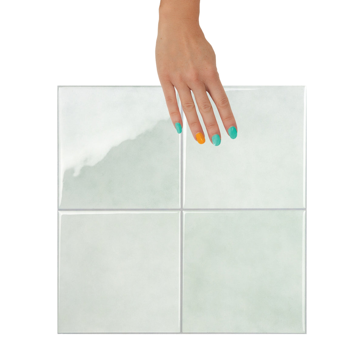 Hand with multicolored nail polish holding a sage green square tile against a white background