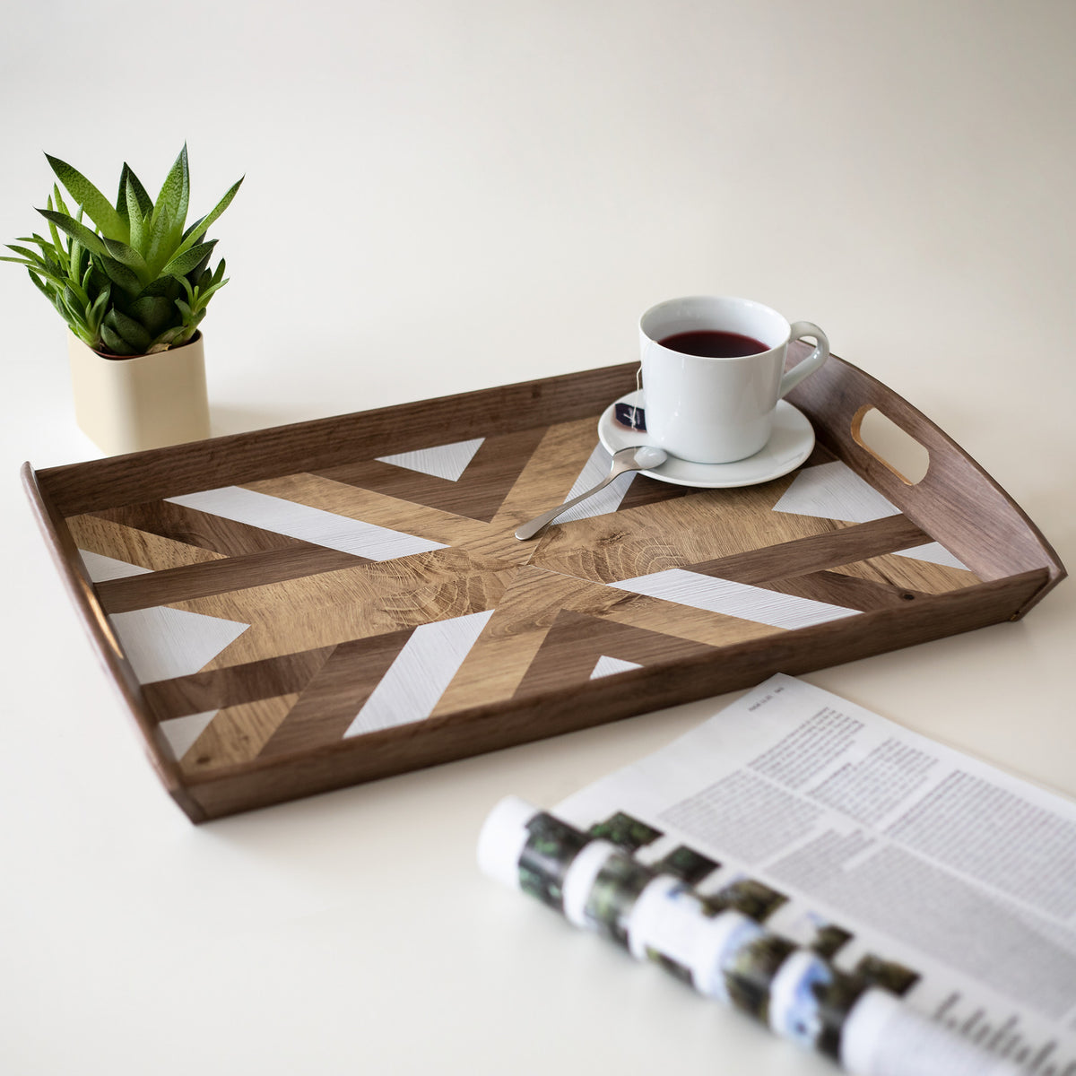 Wooden tray with geometric design, cup of coffee, and magazine on a light surface.