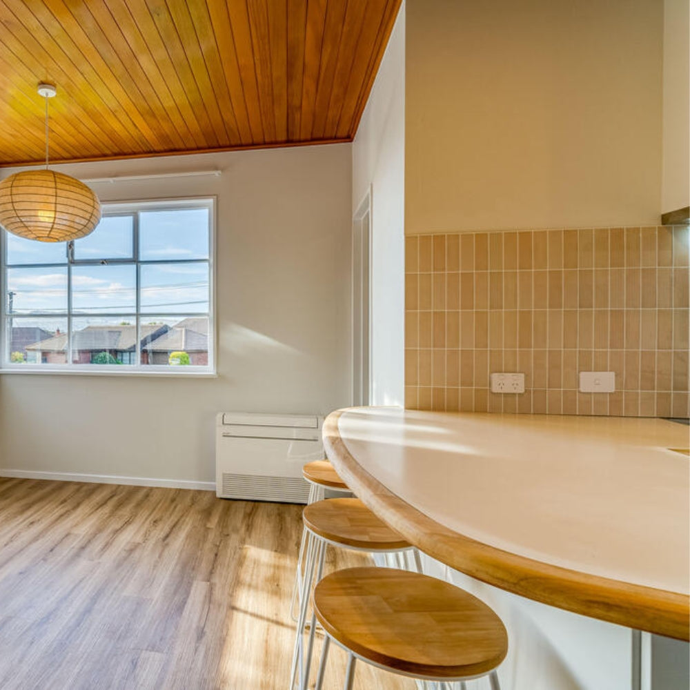 Modern kitchen with wooden ceiling, bar stools, and a window view.
