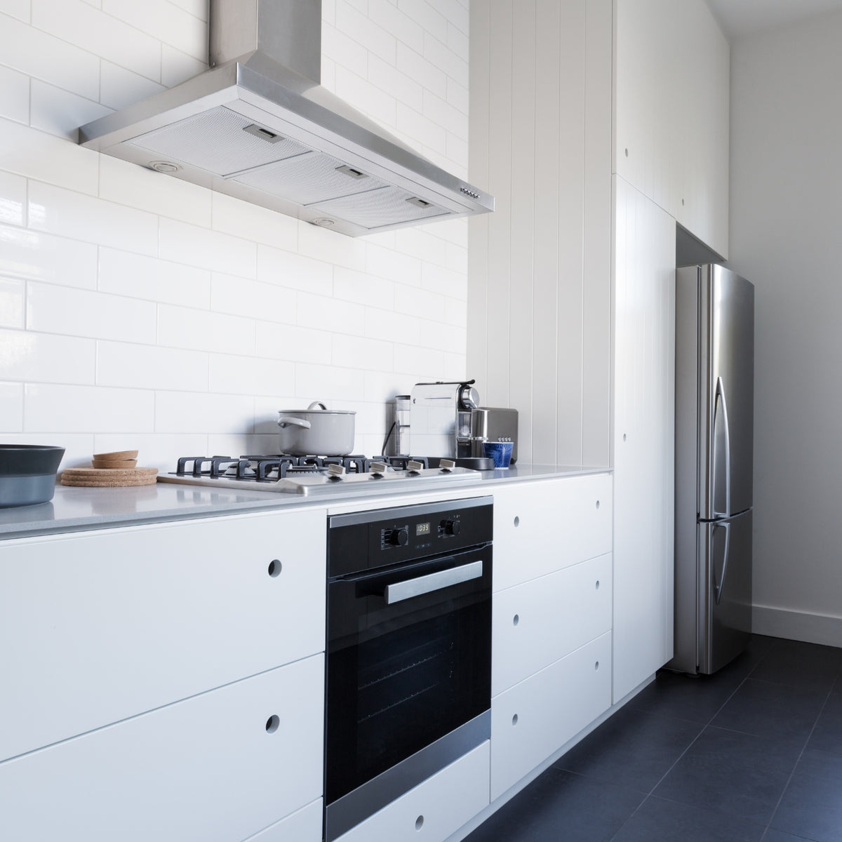 Modern kitchen with white cabinets, stainless steel appliances, and gray tiled floor.