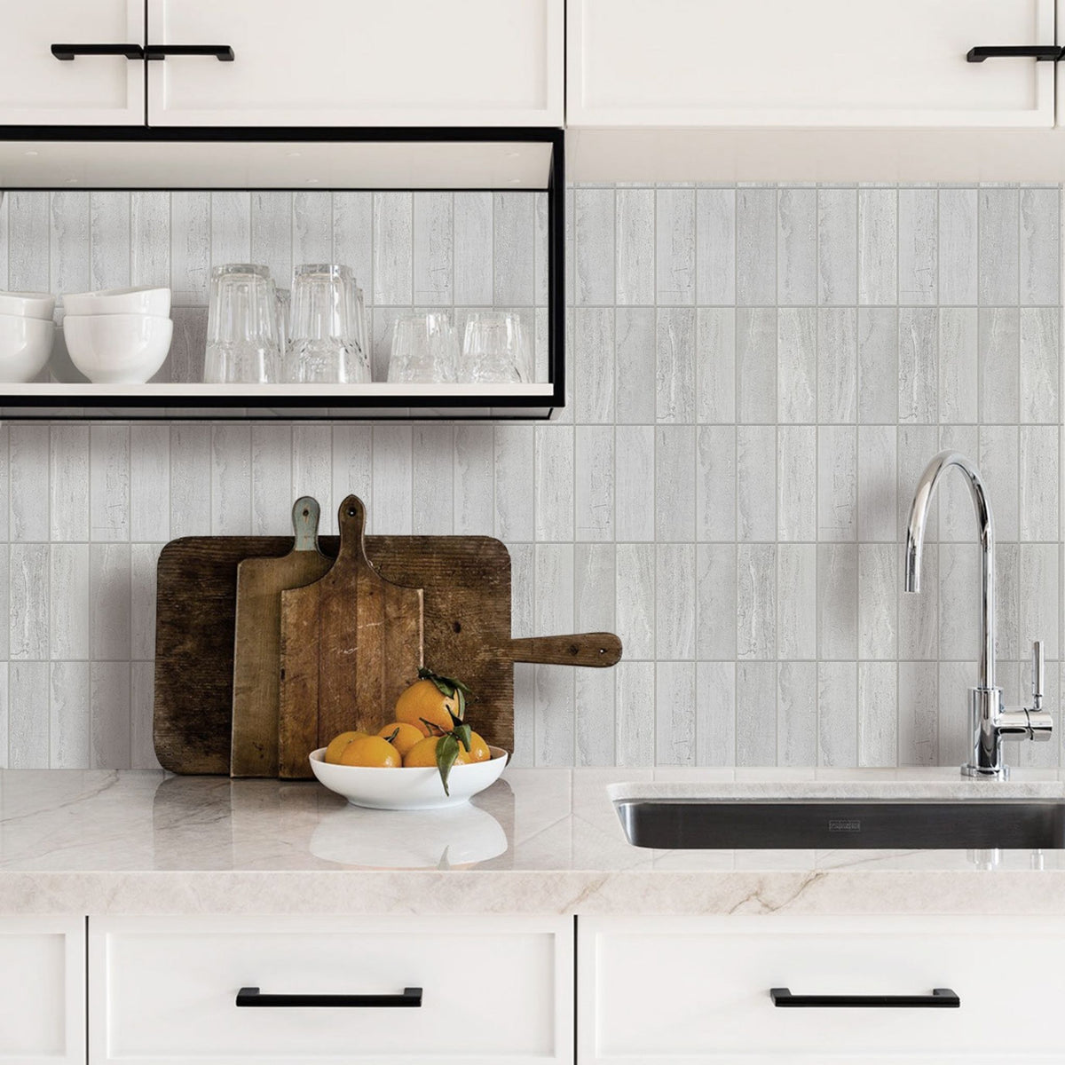 A modern kitchen countertop with a light grey concrete-look tiled backsplash, white cabinets, a chrome faucet, and a bowl of oranges on a marble-like counter.