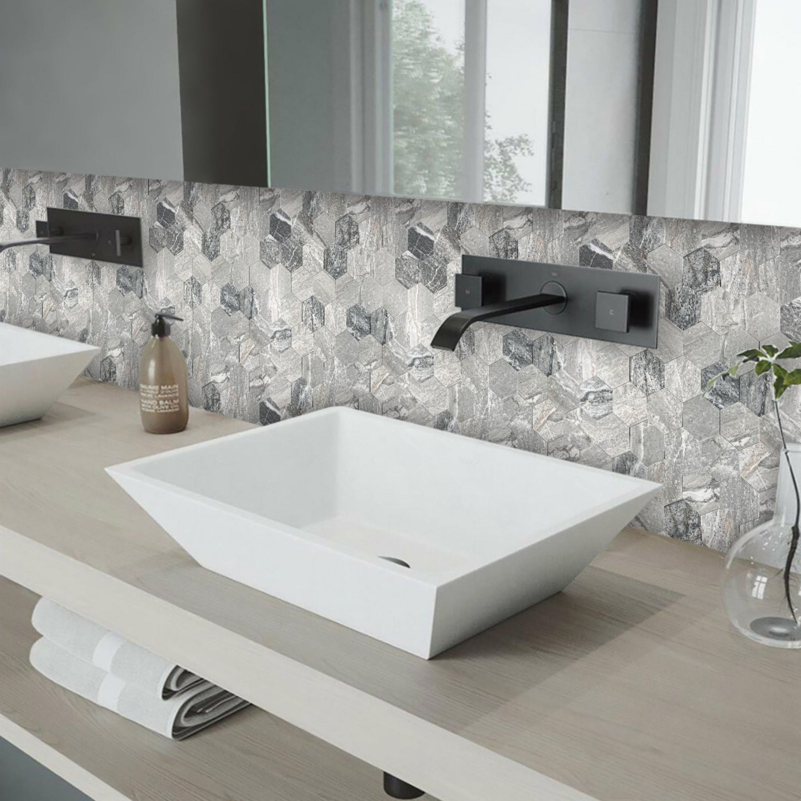 A modern bathroom vanity setup featuring a white rectangular vessel sink, matte black wall-mounted faucet and controls, a grey and white geometric patterned tile backsplash, and a light wood countertop.