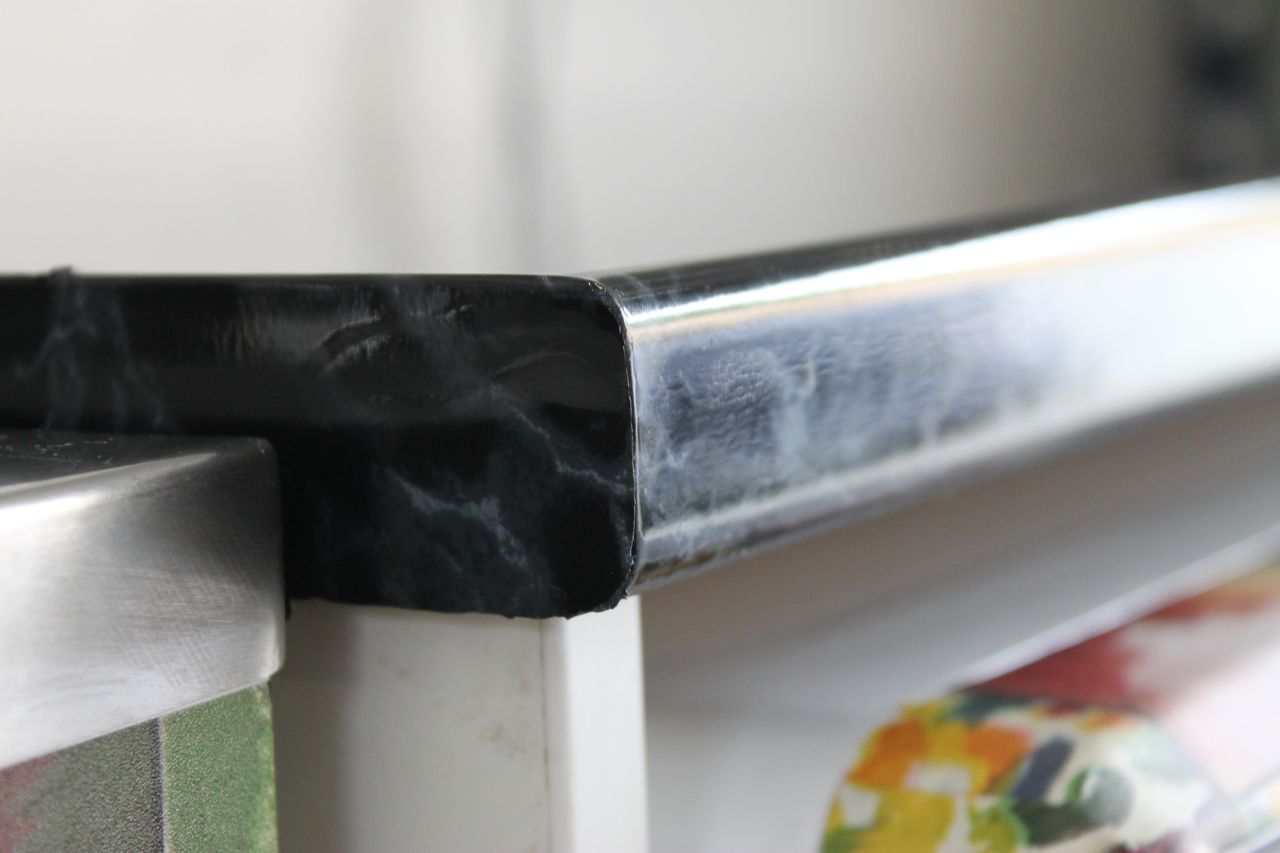 Corner of laundry bench top covered with black marble vinyl