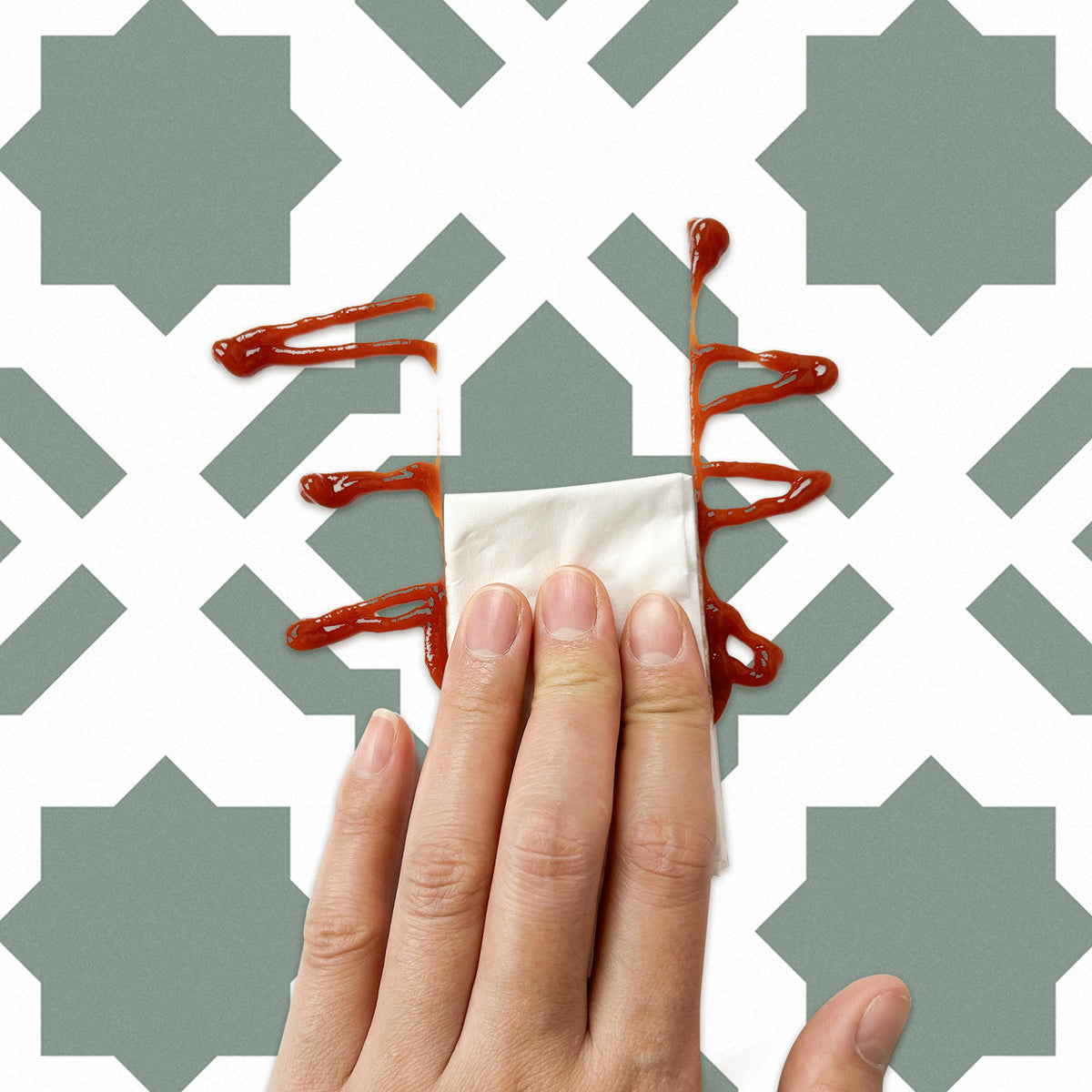 Hand using a paper towel to clean up a small spill of red liquid on a patterned surface.