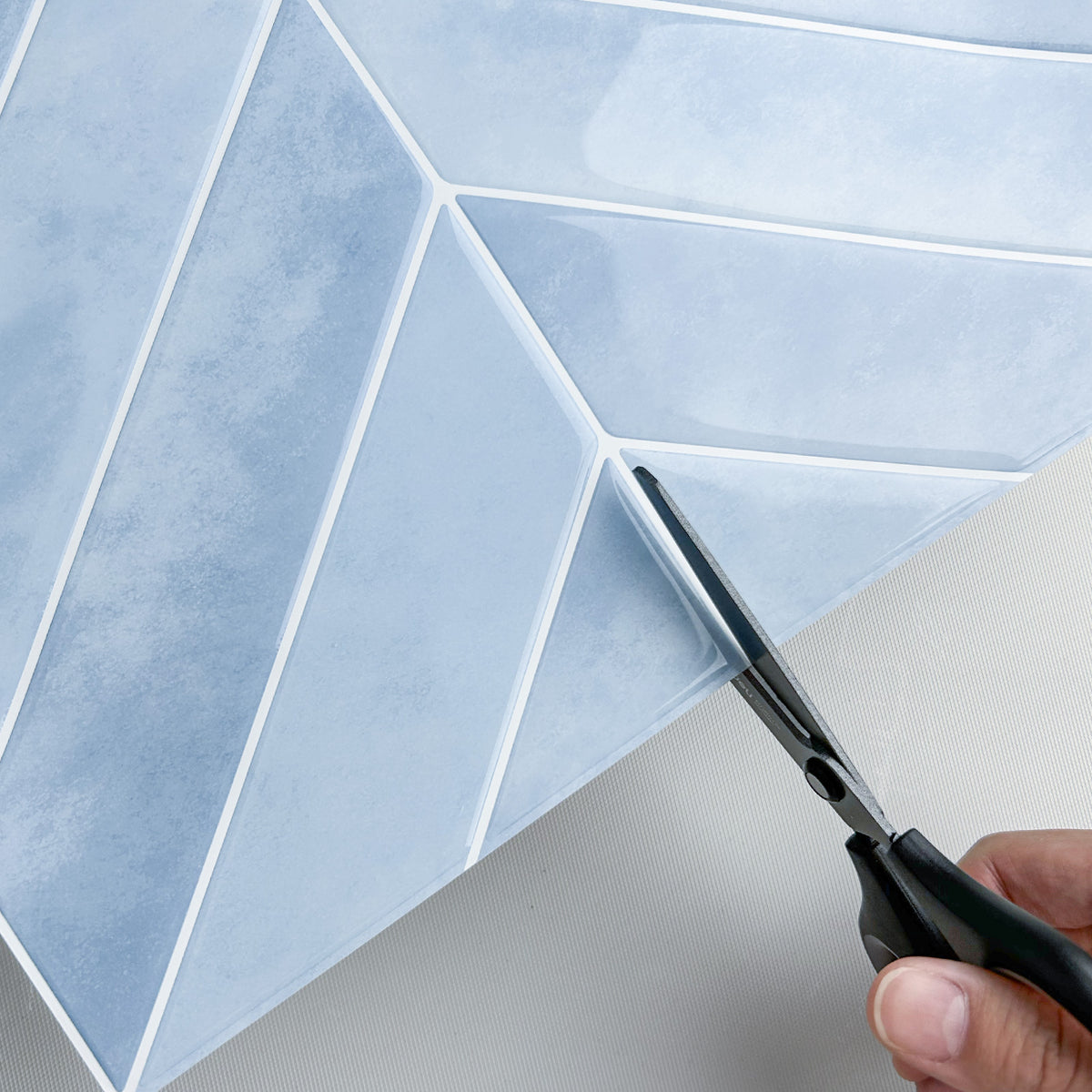 Scissors cutting through a sheet of blue geometric-patterned peel and stick wall tiles