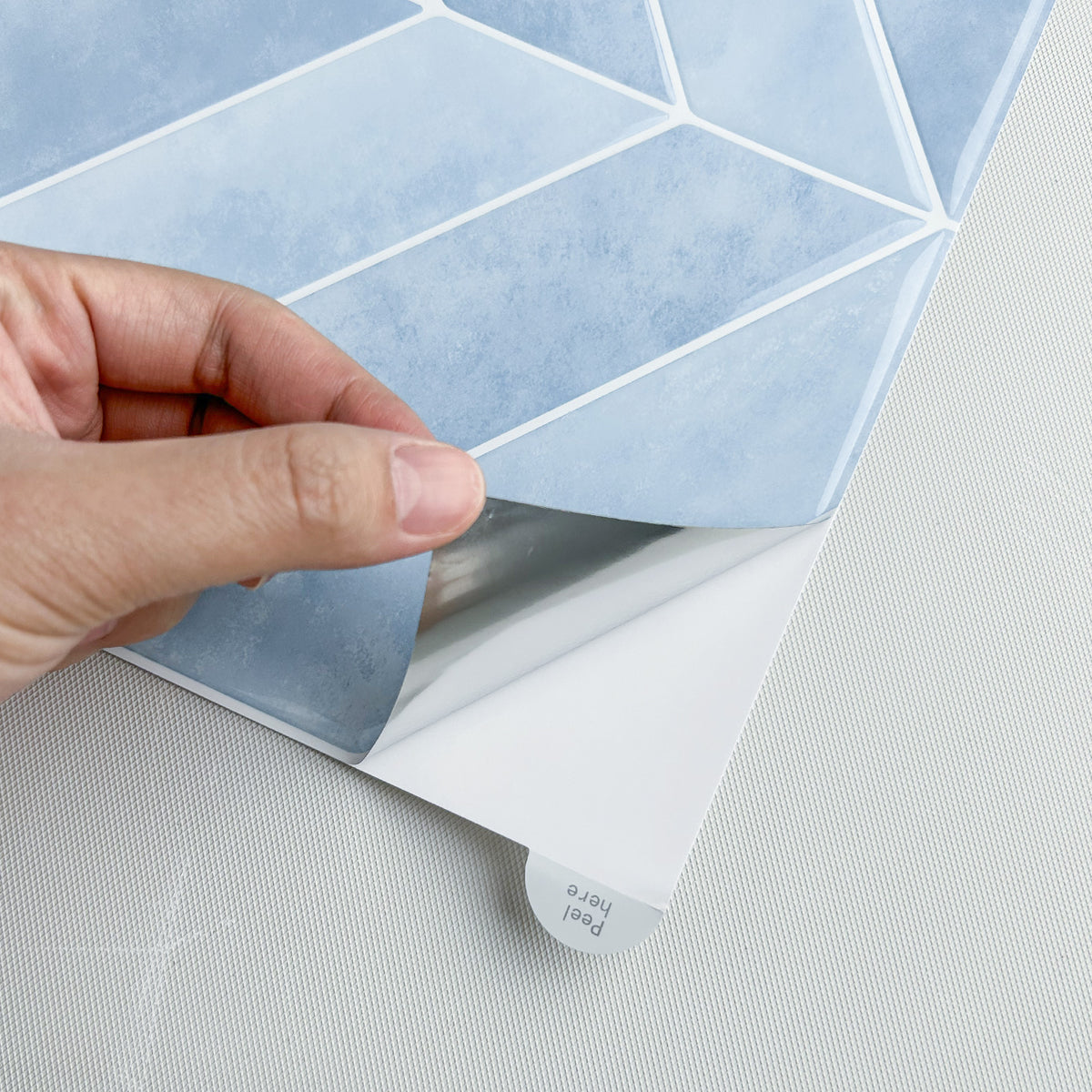 Hand peeling a sheet of blue geometric-patterned vinyl wall tiles from its backing paper.