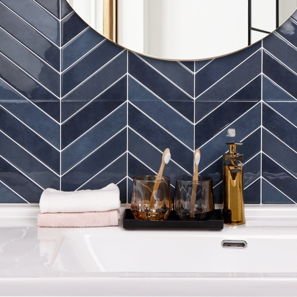 Bathroom counter with towels, glasses, and a mirror against a blue chevron tiled wall.
