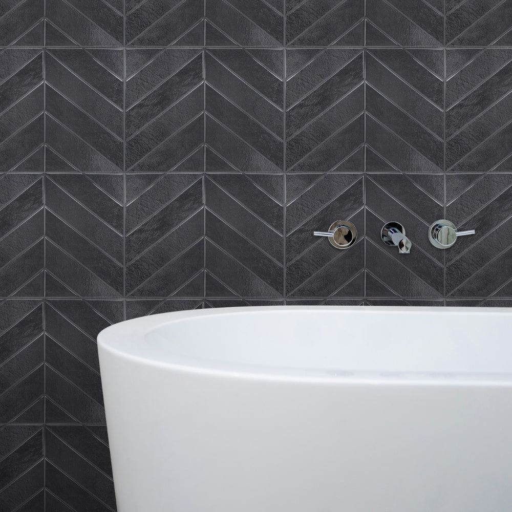 Dark grey-black chevron-patterned tiles on a wall with a white bathtub below.