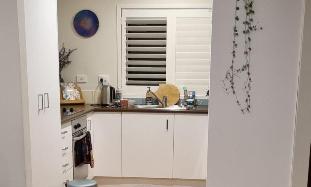 Modern kitchen with white cabinets, stainless steel appliances, and a window with blinds.
