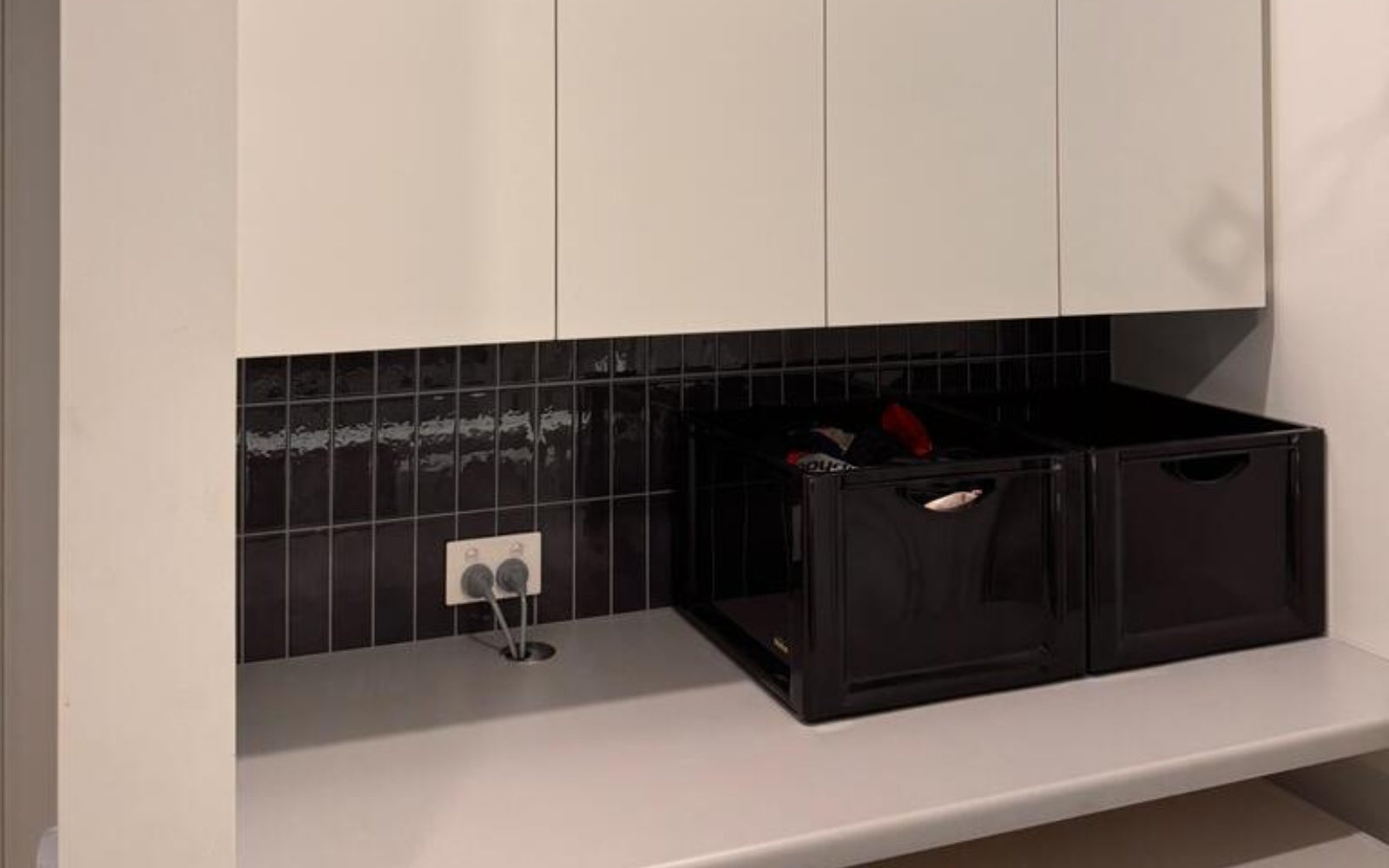 Black storage bins on a white countertop with tiled backsplash