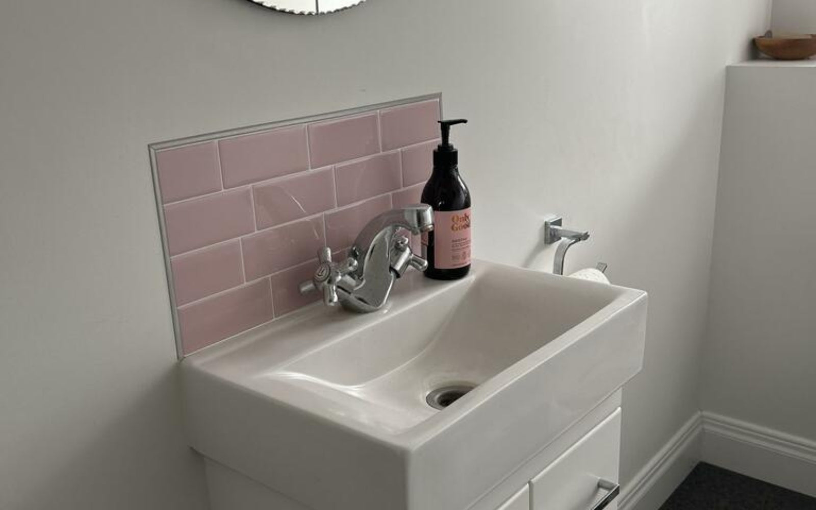 Bathroom sink with pink tiled backsplash and soap dispenser.