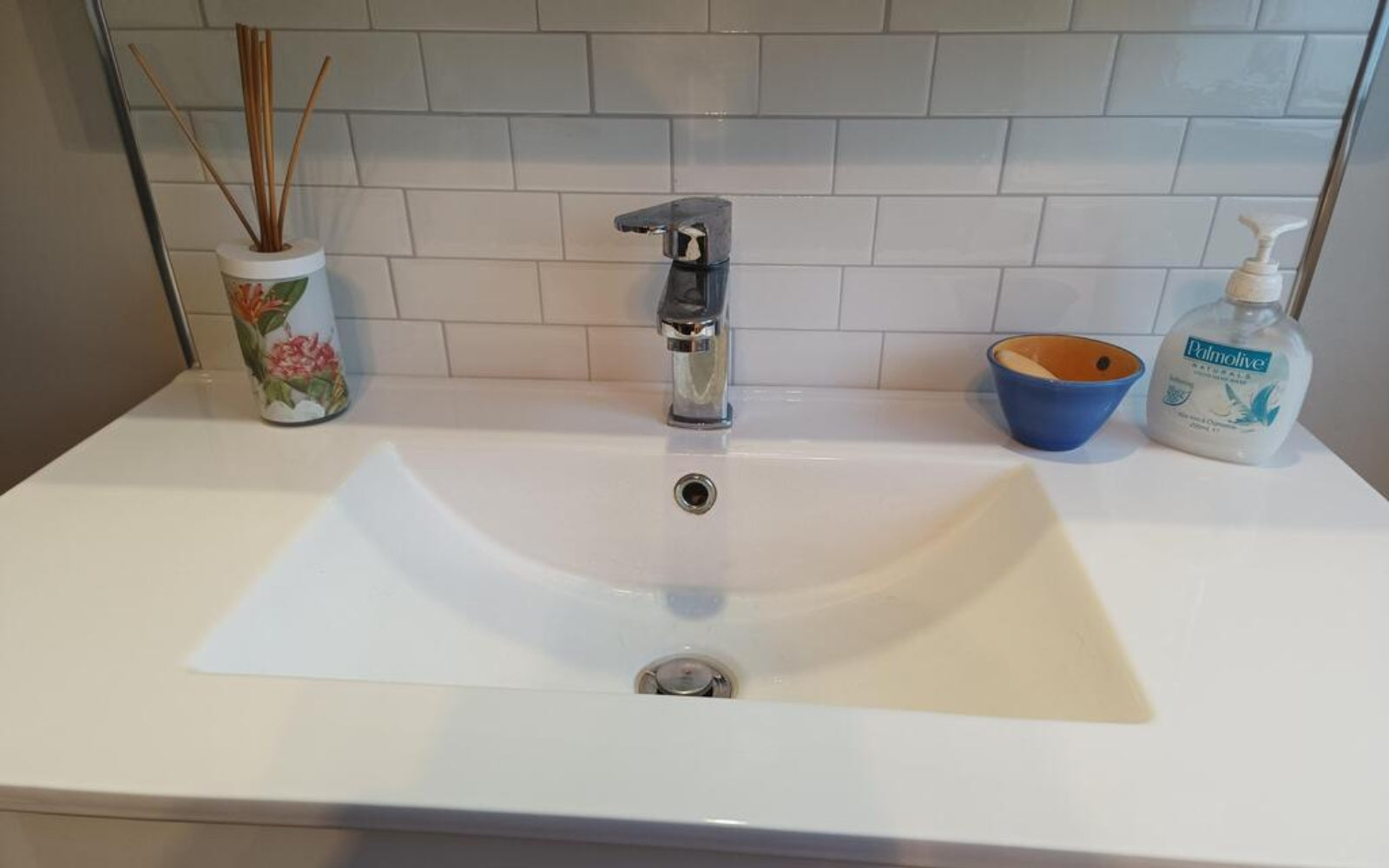 Bathroom sink with faucet, soap dispenser, and decorative items on a tiled wall background.