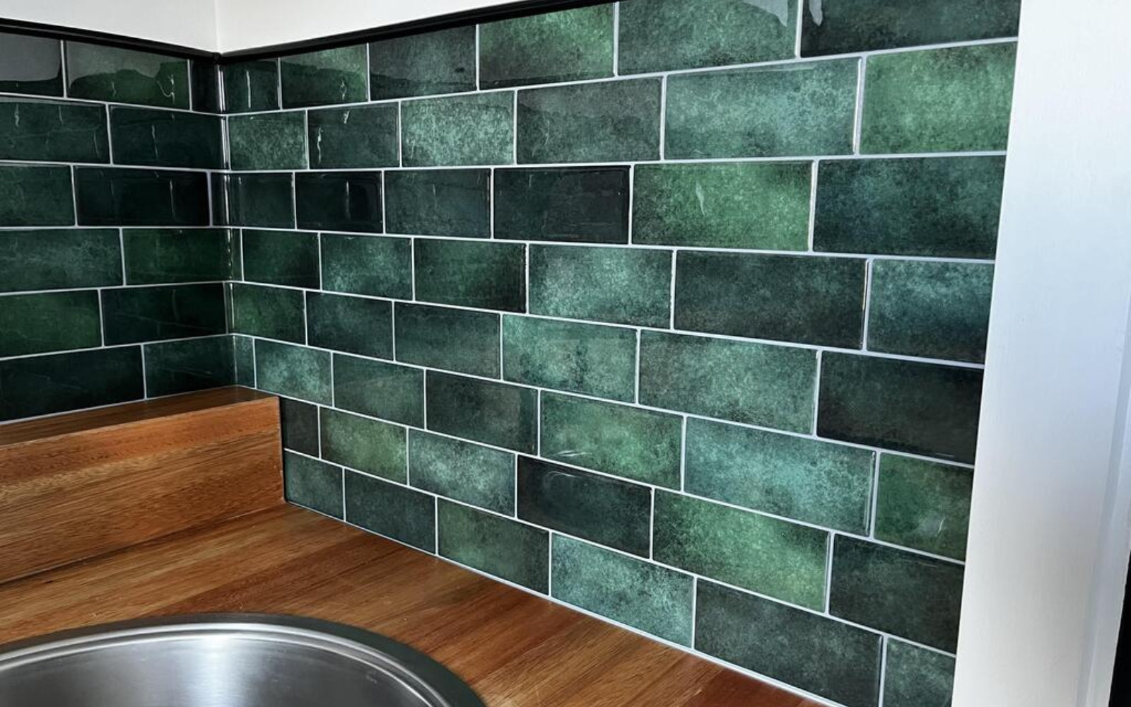 Green tiled wall with a wooden bench and metal sink in a kitchen setting
