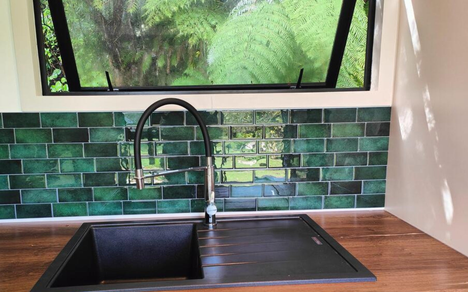 Modern kitchen sink with green tiled backsplash and window view in a campervan