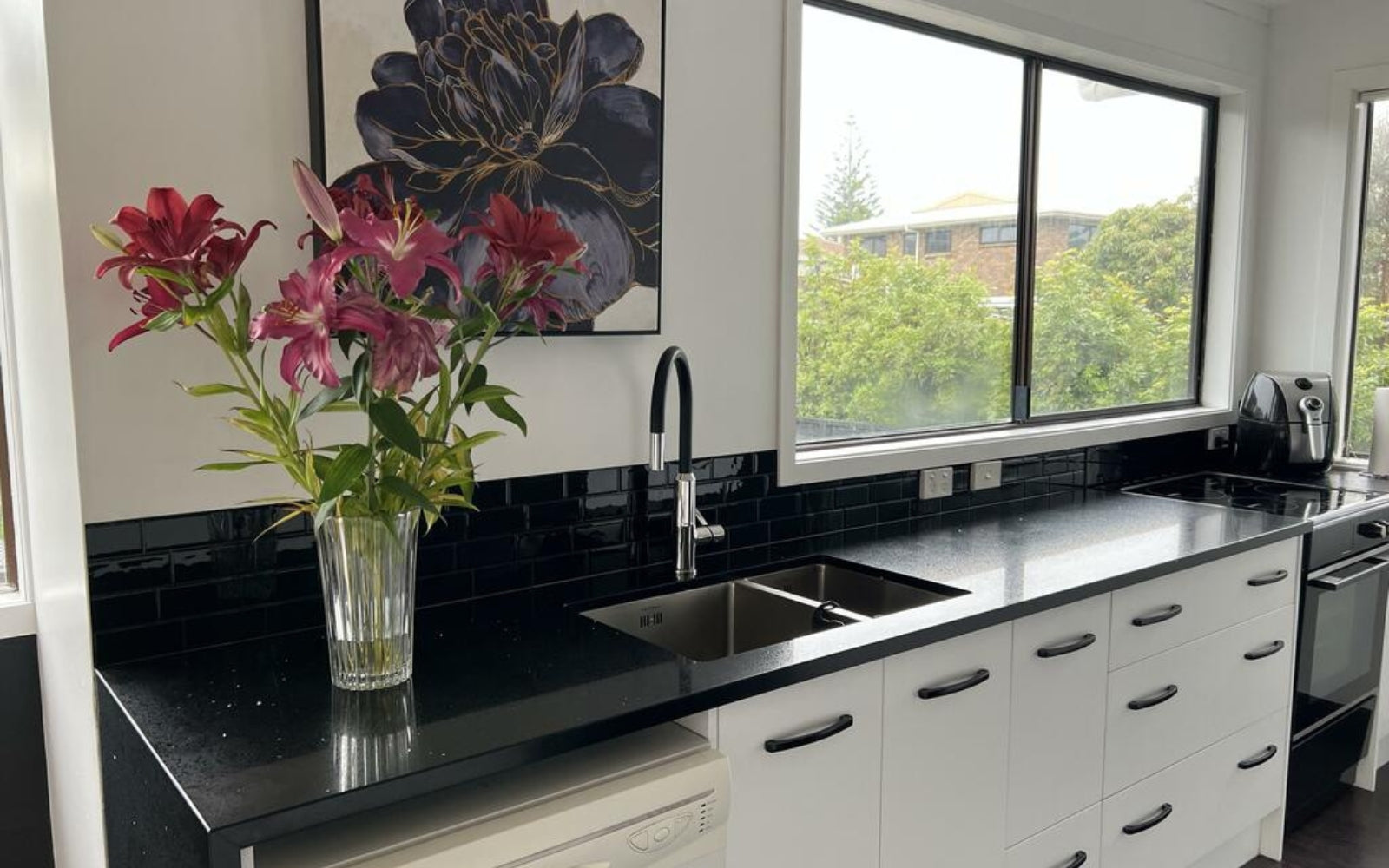 Modern kitchen with black splashback, countertops, white cabinets, and a vase of flowers.