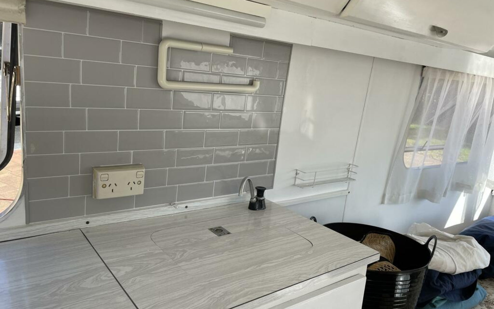 Kitchen area with grey self-adhesive tiled backsplash and wooden countertop in a vehicle interior.