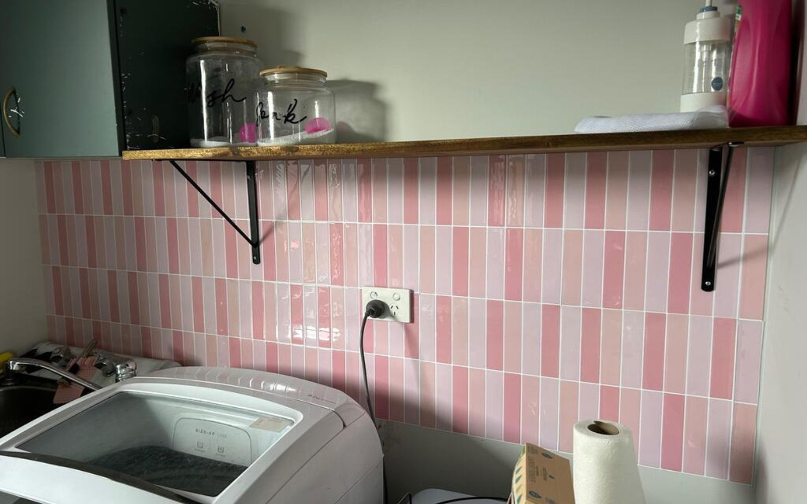 Kitchen with pink tiled wall, washing machine, and shelves with jars.