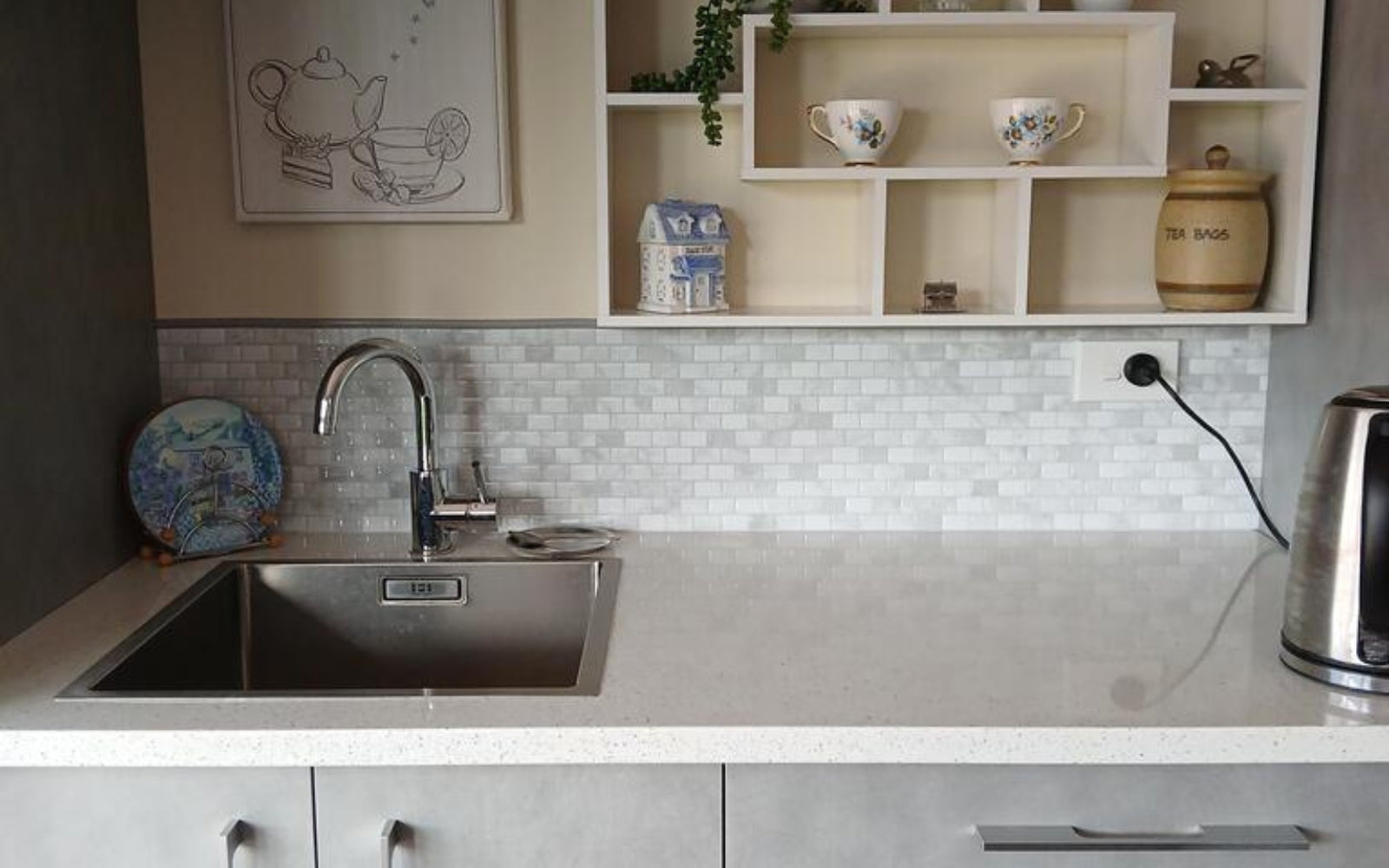 Modern kitchen with stainless steel sink, countertop, tiled splashback and shelves with decorative items.