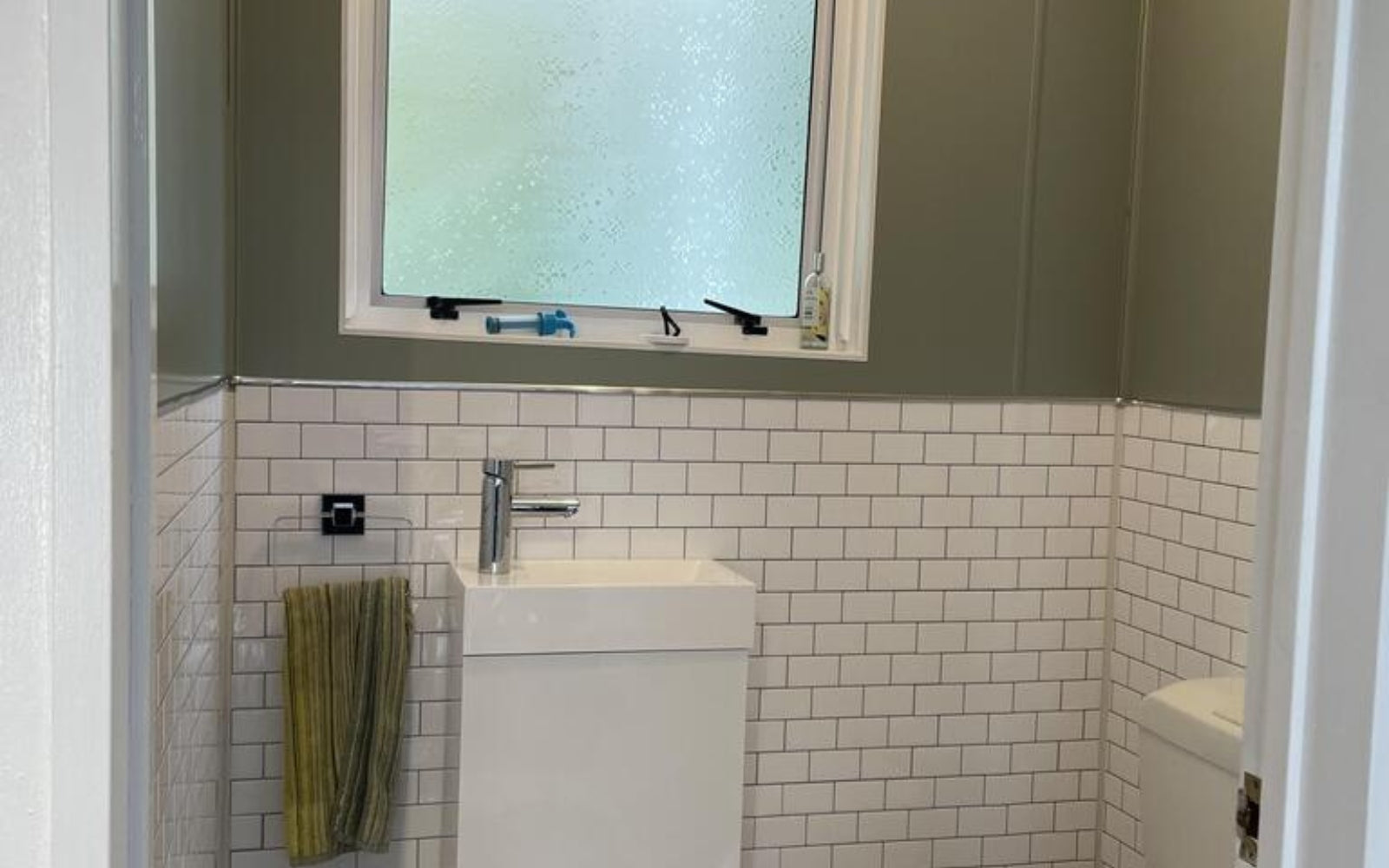 Bathroom with white tiled walls, a sink, and a window with frosted glass.