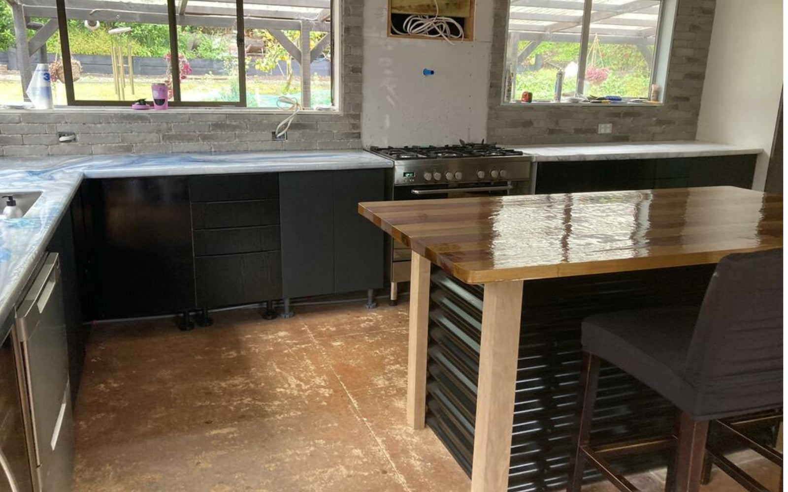Modern kitchen with black vinyl wrapped cabinets, stainless steel appliances, and a wooden island.