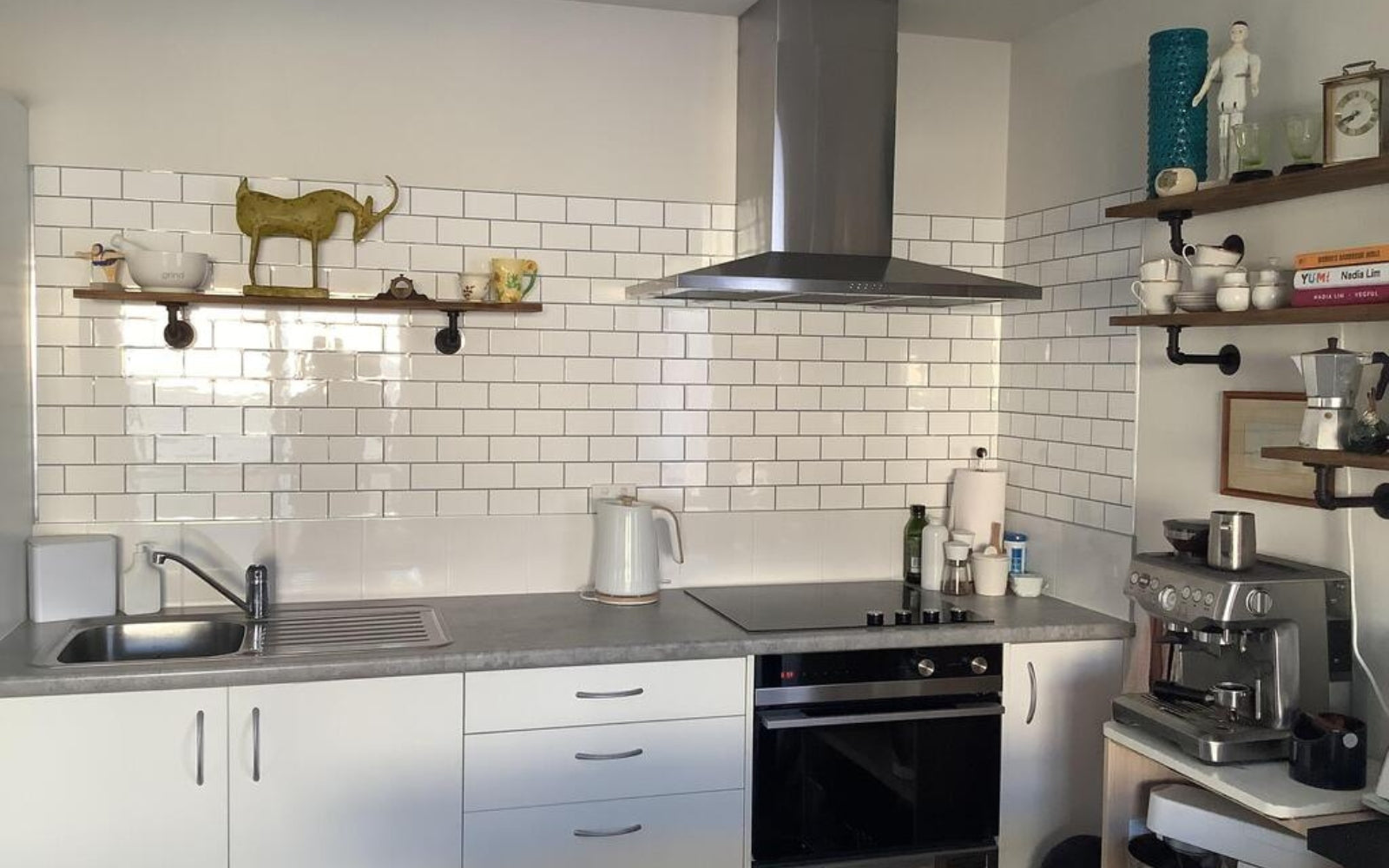Modern kitchen with white tiled backsplash, stainless steel appliances, and wooden shelves.