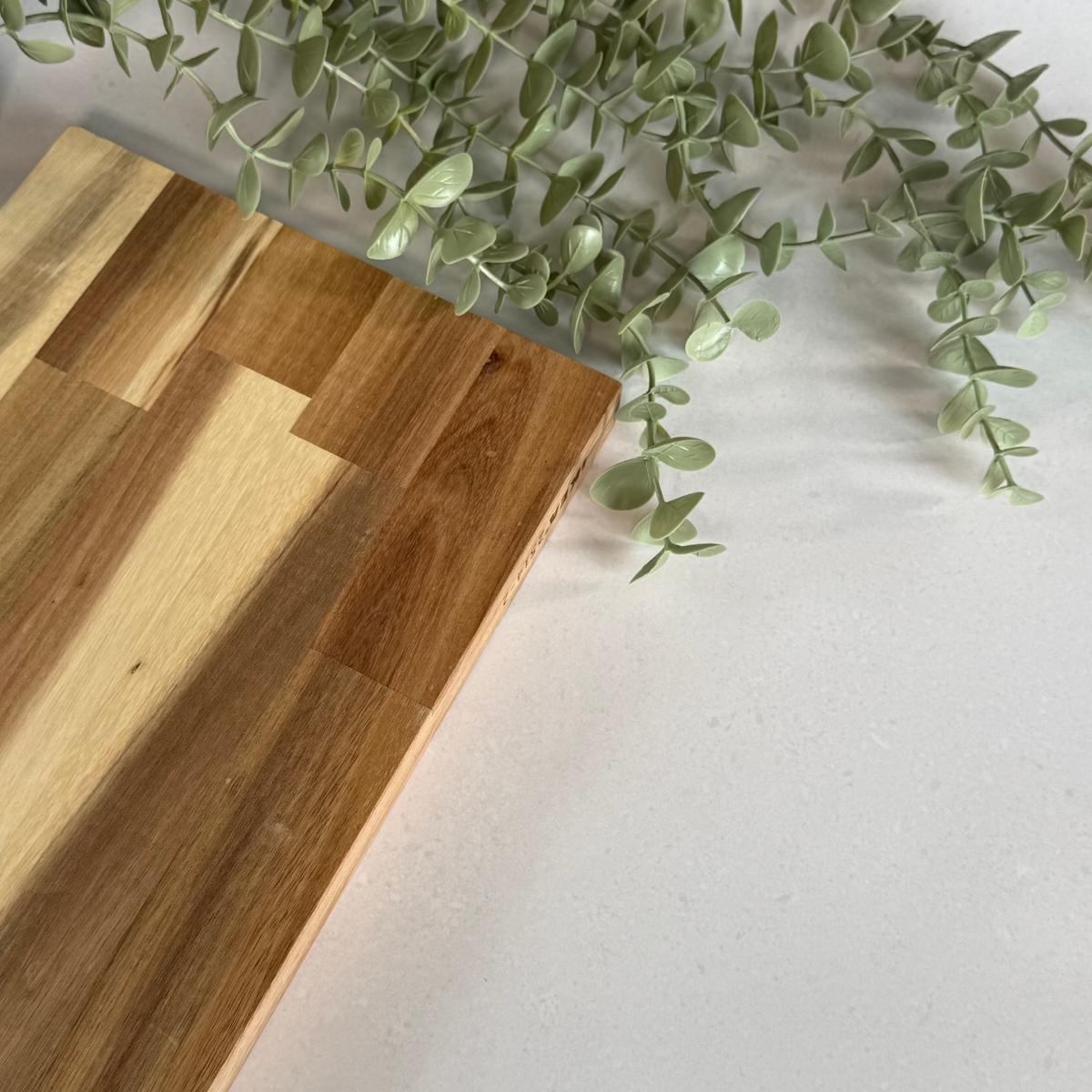 Wooden cutting board on a white quartz vinyl wrapped benchtop with a green plant in the corner