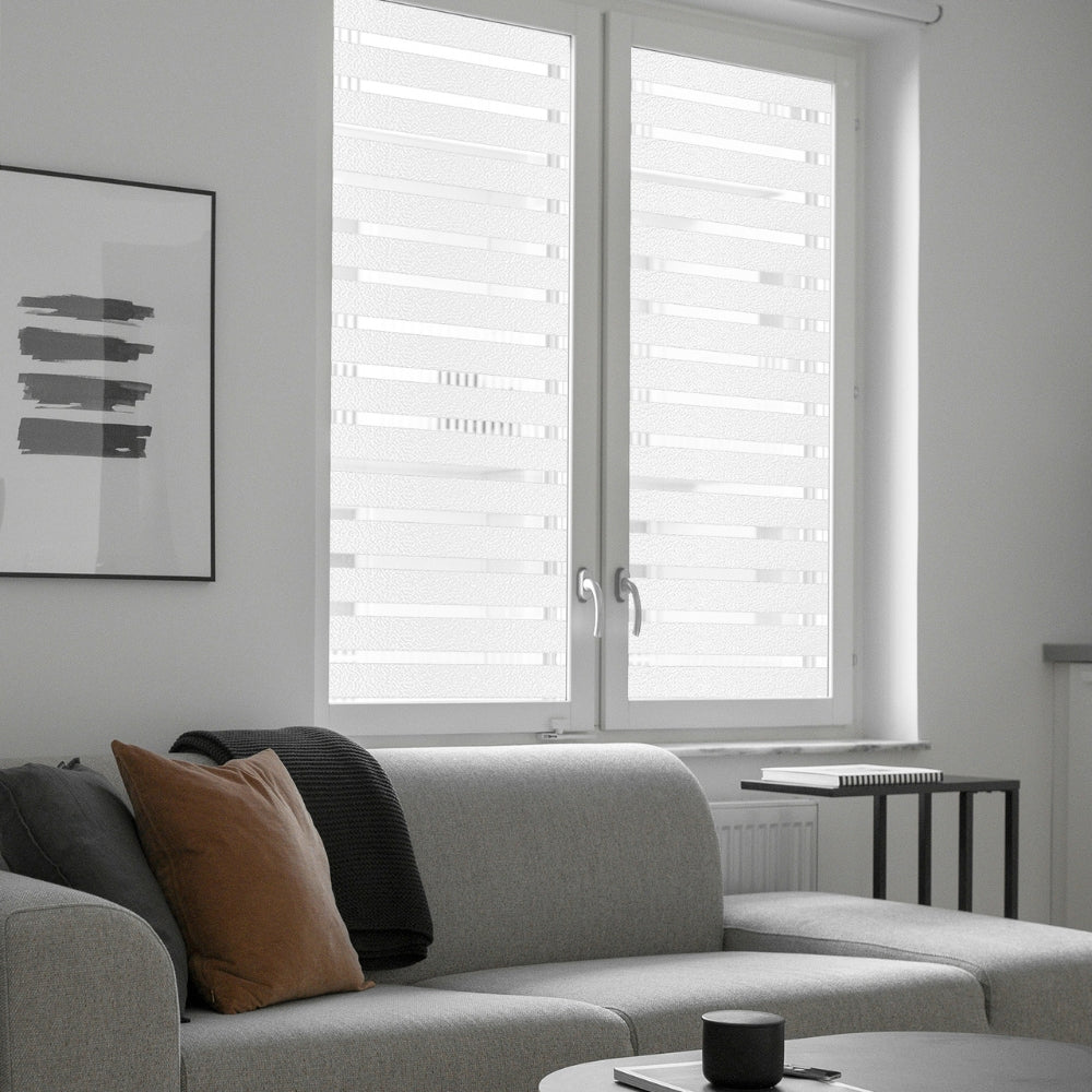 Modern living room with a grey sofa, coffee table, and frosted stripes window film covered windows.