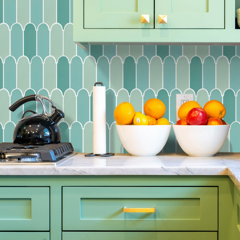 Kitchen counter with bowls of fruit against a green tiled backsplash.