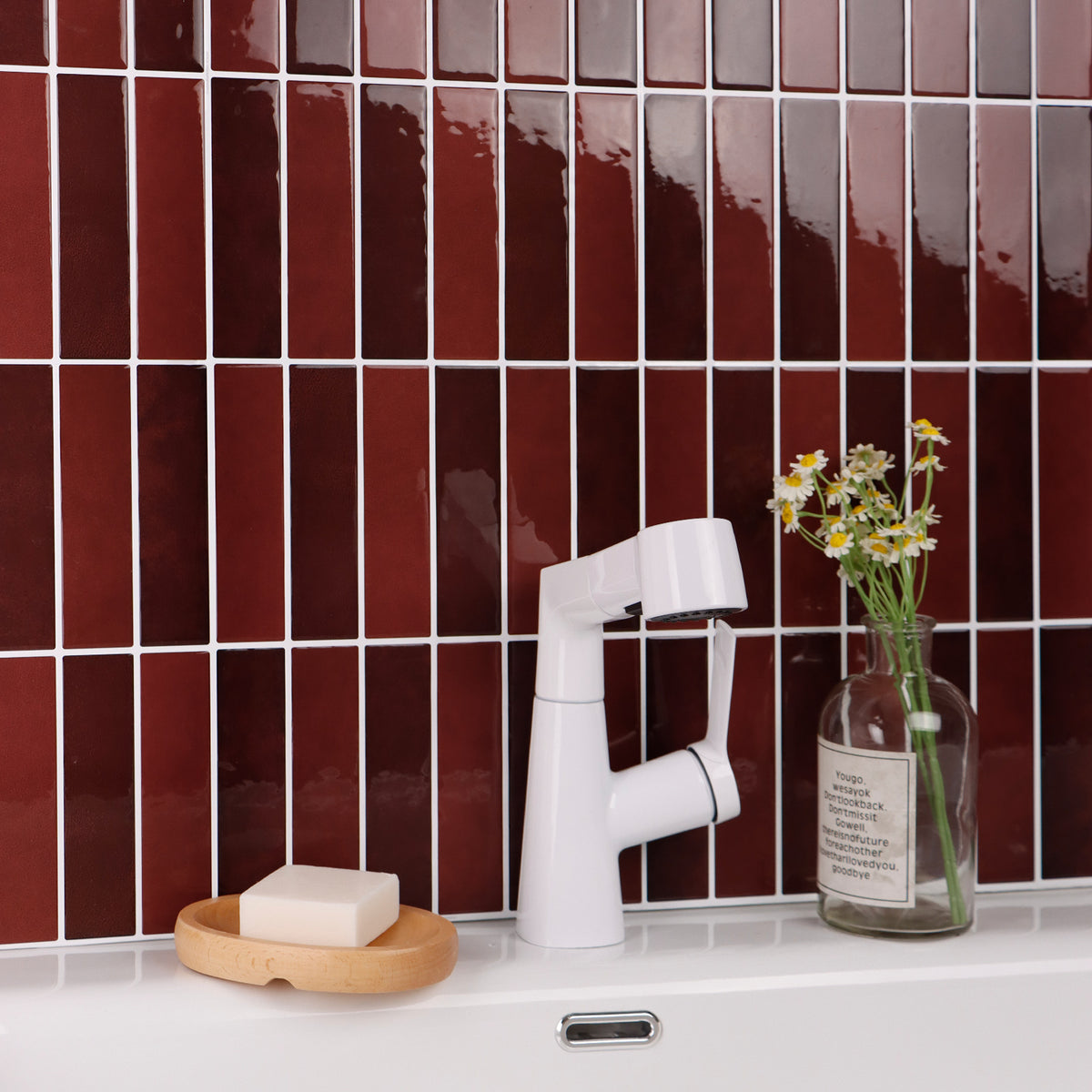 White faucet with a soap bar and vase against a red burgundy kit kat tiled wall