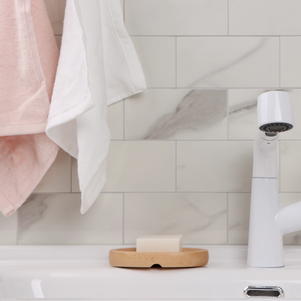 White bathroom faucet on a white vanity with candles and a plant in the background