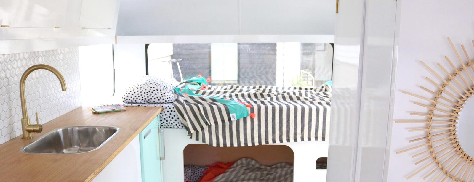 Caravan kitchen to left with hexagon peel and stick wall tiles, wooden benchtop and mint vinyl wrapped fridge and brass tap , to the right a bunkbed