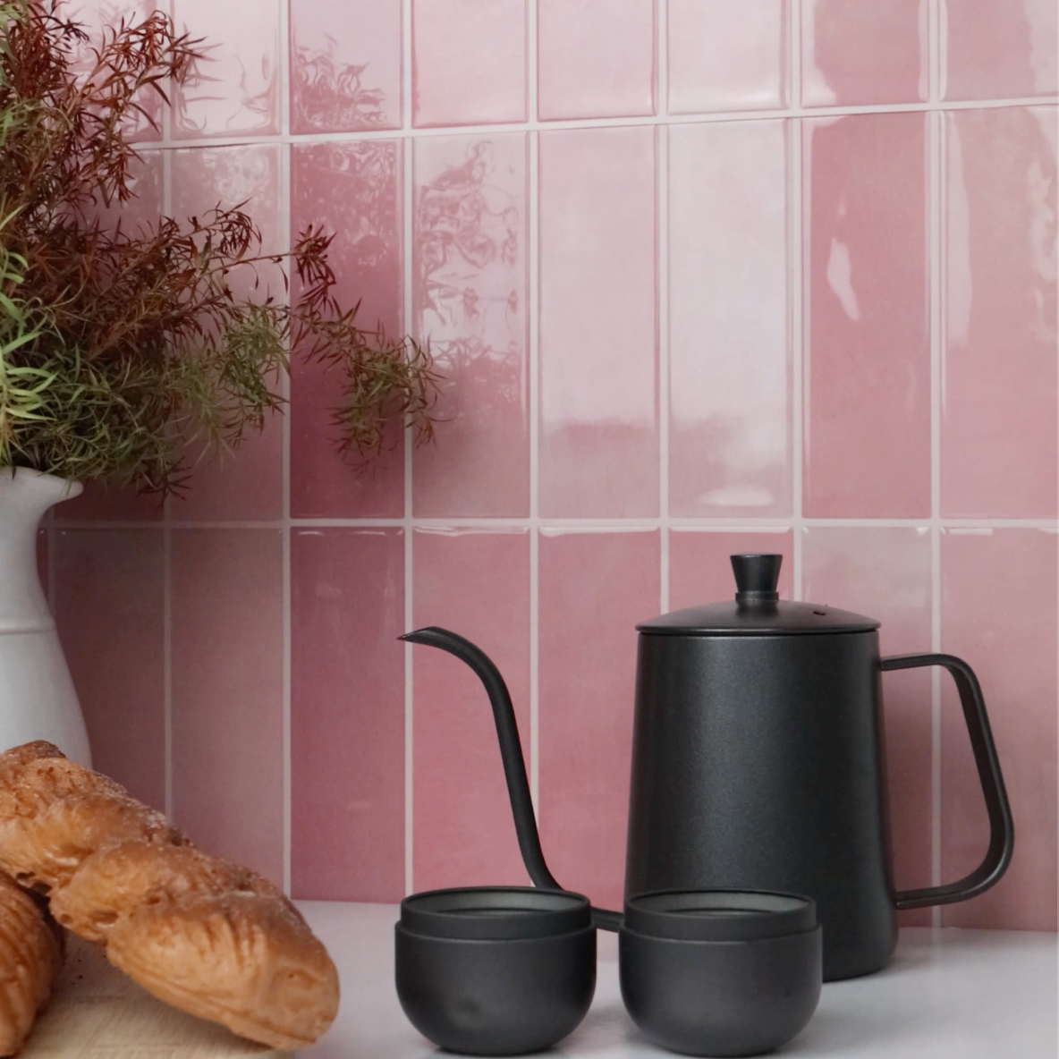 Black teapot and cups on a white surface with pink tiled wall in the background