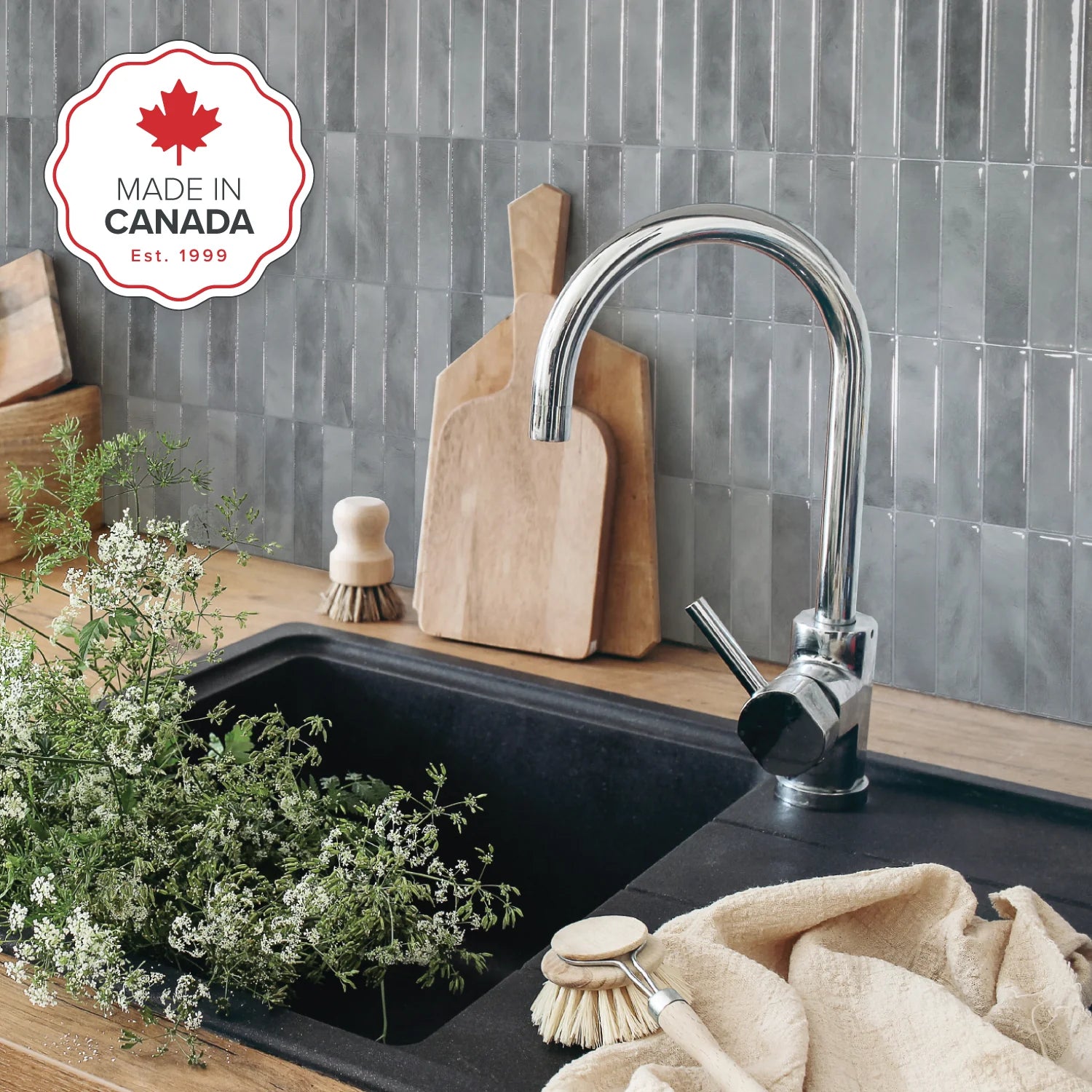Kitchen sink with faucet, cutting boards, and cleaning supplies on a tiled wall background with 'Made in Canada' logo.