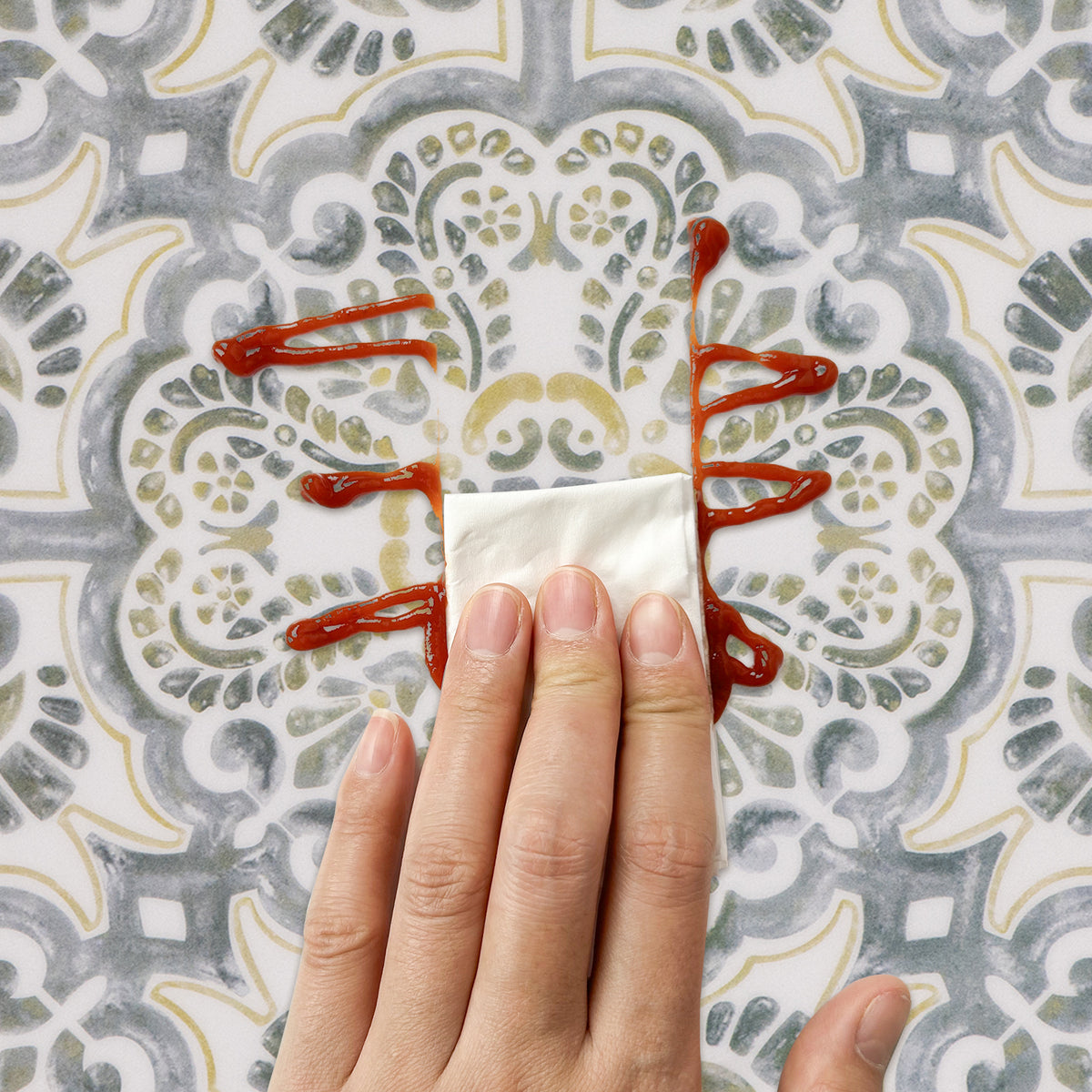 Hand holding a piece of paper with red sauce on a patterned floor tile