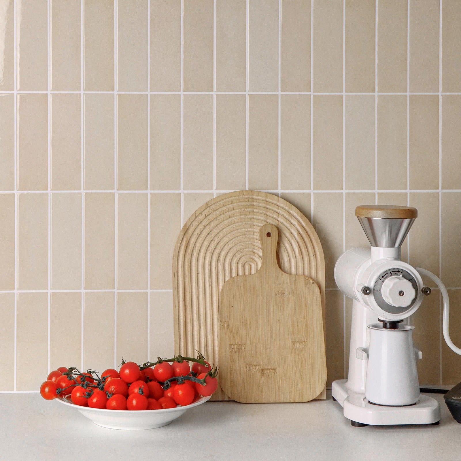 Kitchen counter with a bowl of tomatoes, wooden cutting board, and white appliance against a tiled wall.